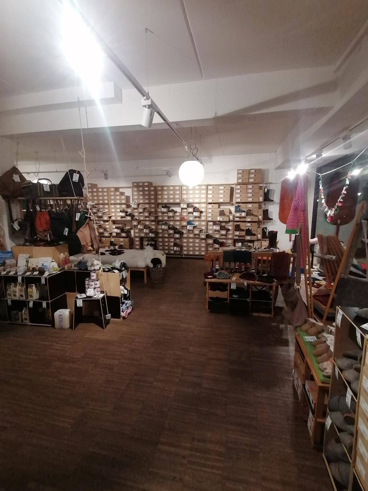 Geräumiger Verkaufsraum mit Holzfußboden, Regalen voller Schuhe und verschiedenen Auslagen unter heller Beleuchtung.