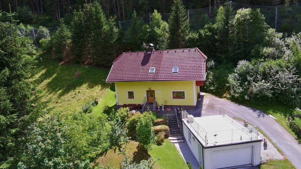 Panoramablick auf ein freistehendes Haus mit Garage und Dachterrasse, umgeben von Wald und Bergen.