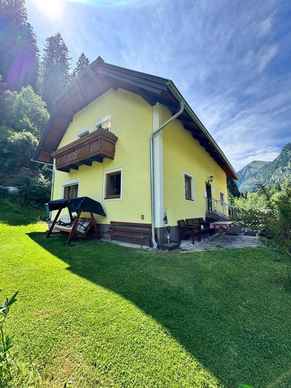 Rückseite des Hauses mit kleiner Terrasse, Gartenmöbeln, Schaukel und großem, sonnigen Rasen.