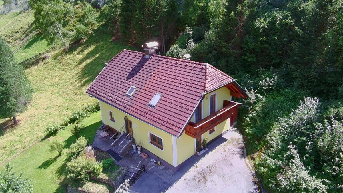 Luftaufnahme des Hauses mit rotem Ziegeldach, gelber Fassade, Garage und weitläufigem Grundstück.