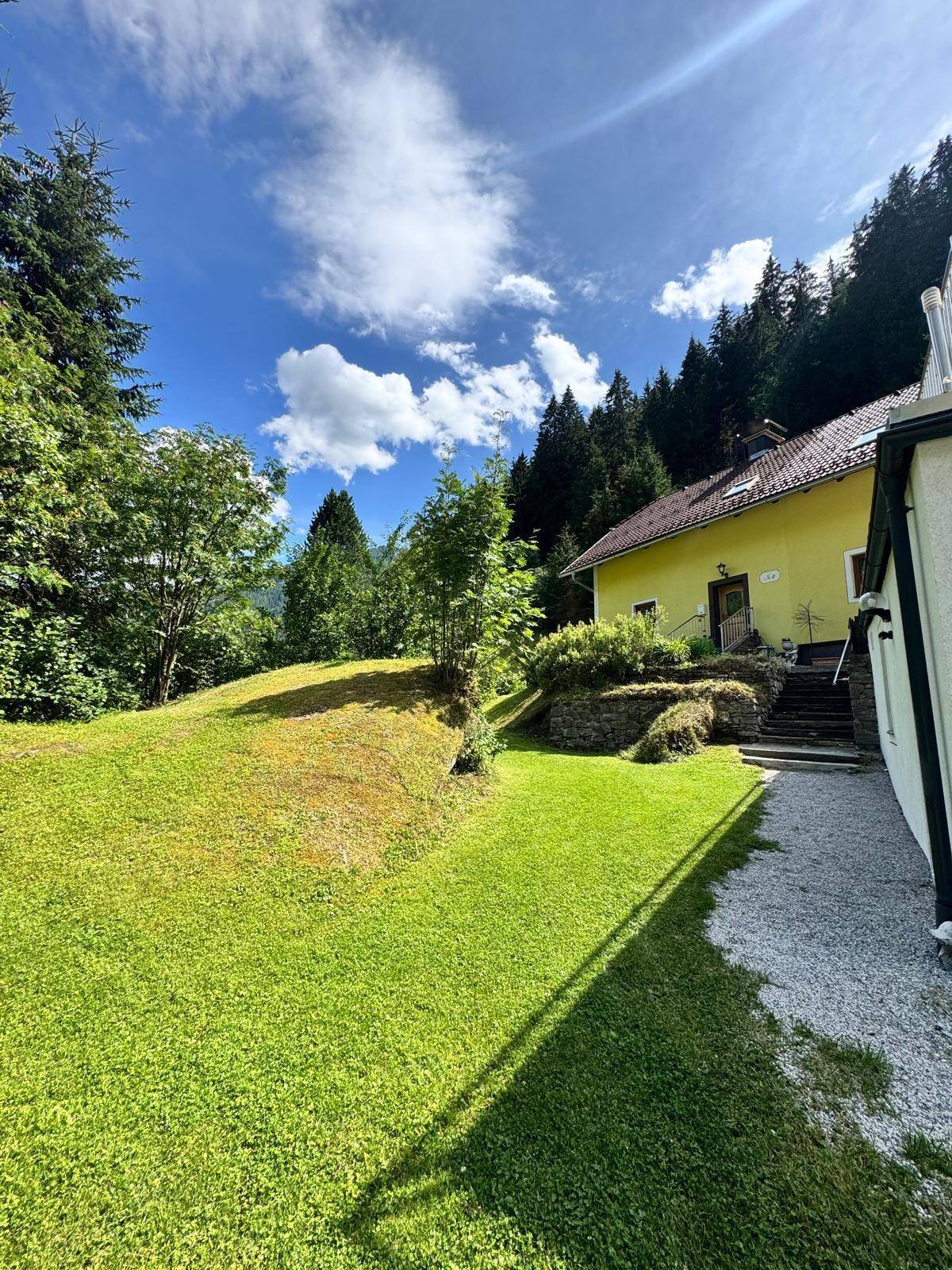 Großer, gepflegter Gartenbereich mit Rasenfläche und Blick auf die bewaldeten Hügel und Berge.