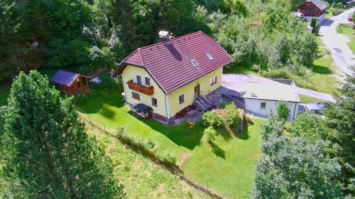Weitläufige Luftaufnahme des Hauses mit Garten, Garage, Dachterrasse und umgebender Naturlandschaft.