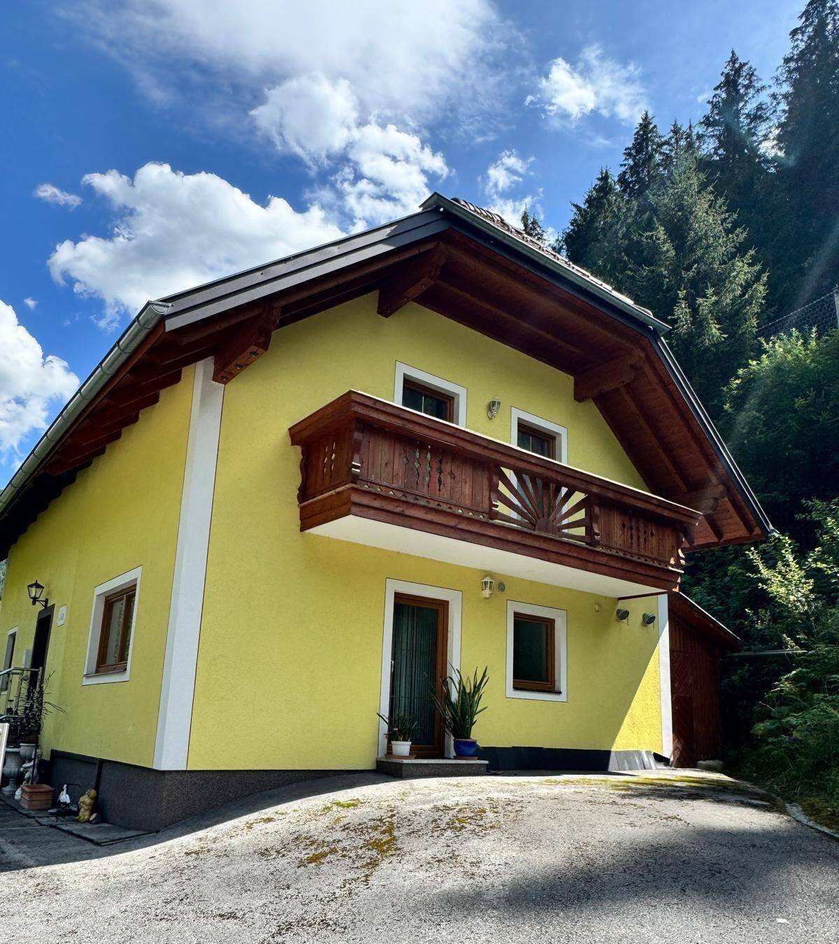 Detailansicht der gelben Hausfassade mit traditionellem Holzbalkon und Eingangstür.