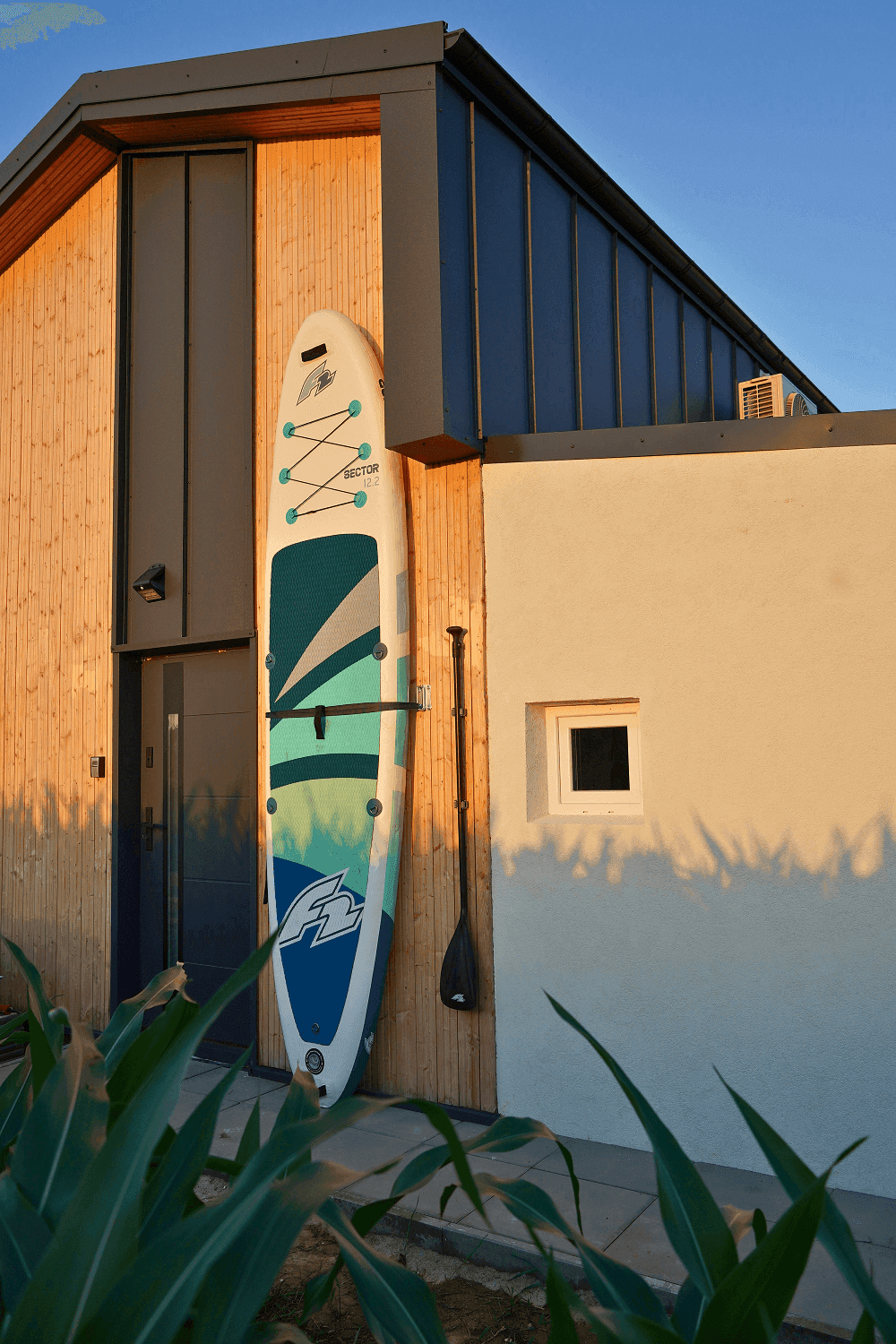 Außenwand eines modernen Hauses mit Holzverkleidung und einem Stand-Up-Paddleboard.