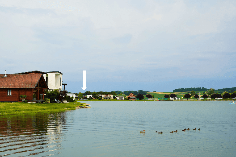 Panoramablick auf den See mit umliegenden Häusern und einer Markierung auf ein bestimmtes Objekt.