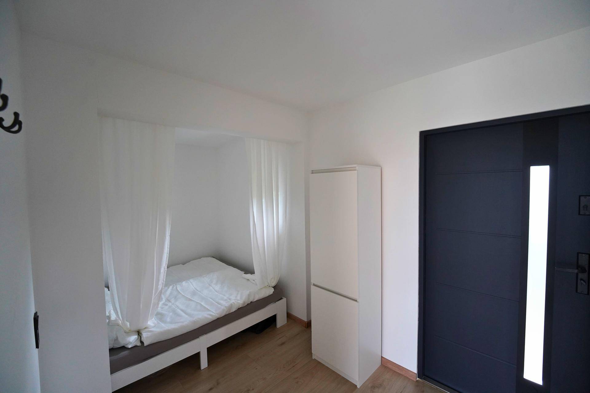 Kleines Schlafzimmer oder Gästezimmer mit Bett in einer Nische und weißem Kleiderschrank.