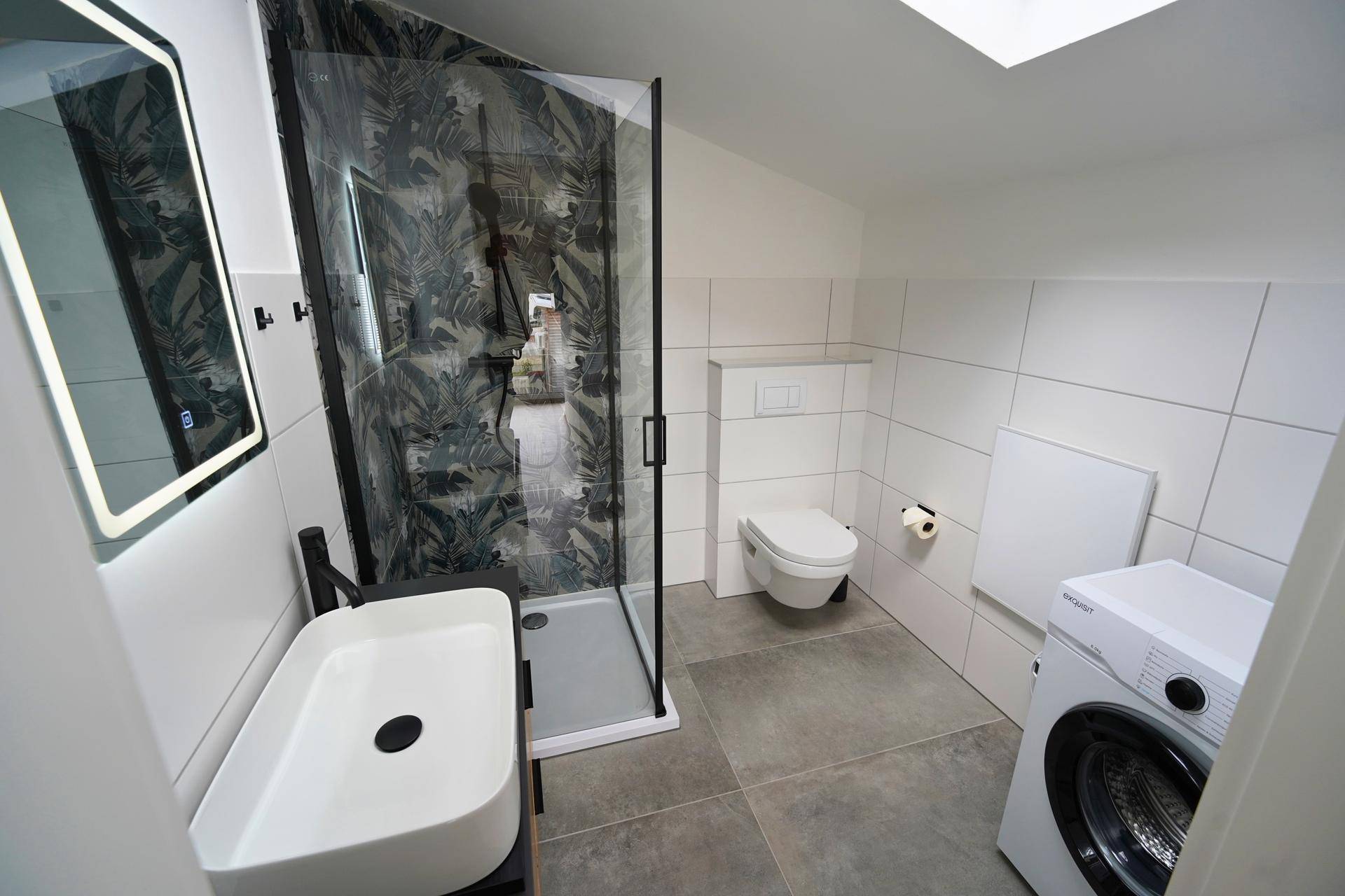 Modernes Badezimmer mit begehbarer Dusche, Waschbecken und Waschmaschine unter Dachschräge.