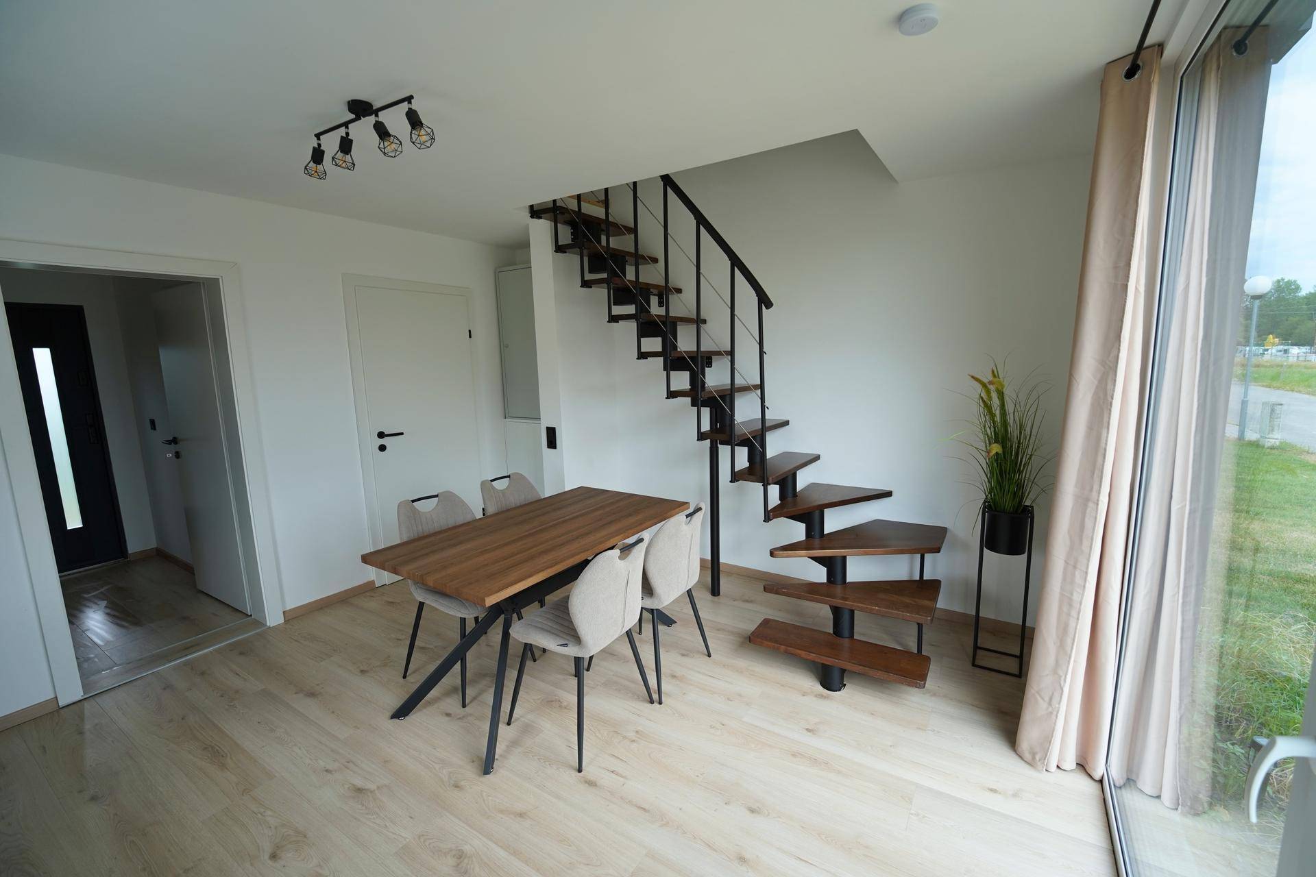 Heller Essbereich mit Holztisch, modernen Stühlen und einer offenen Treppe zum Obergeschoss.