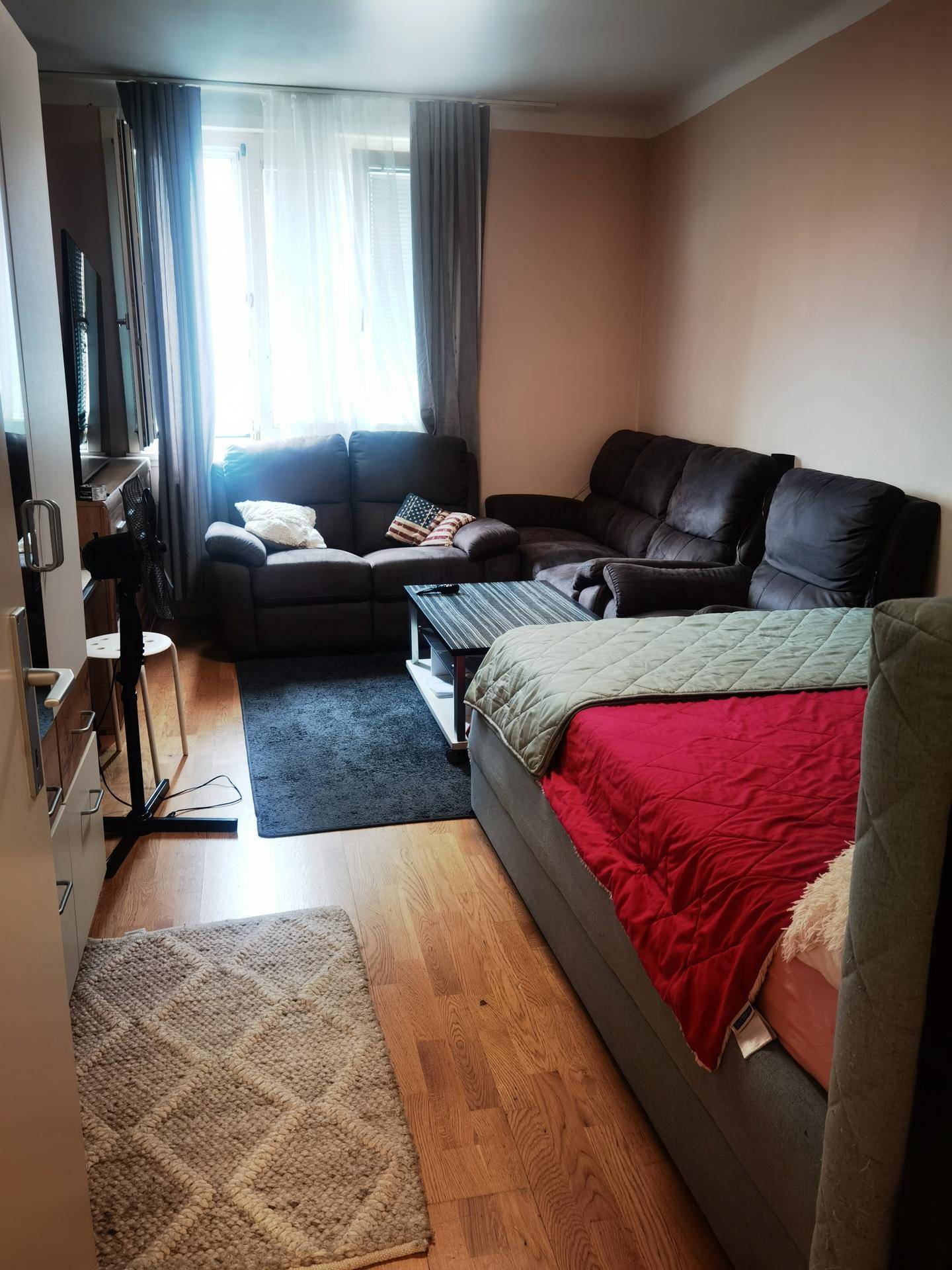 Wohnzimmer mit Sofa, Couchtisch und einem Bett, hell durch große Fenster.