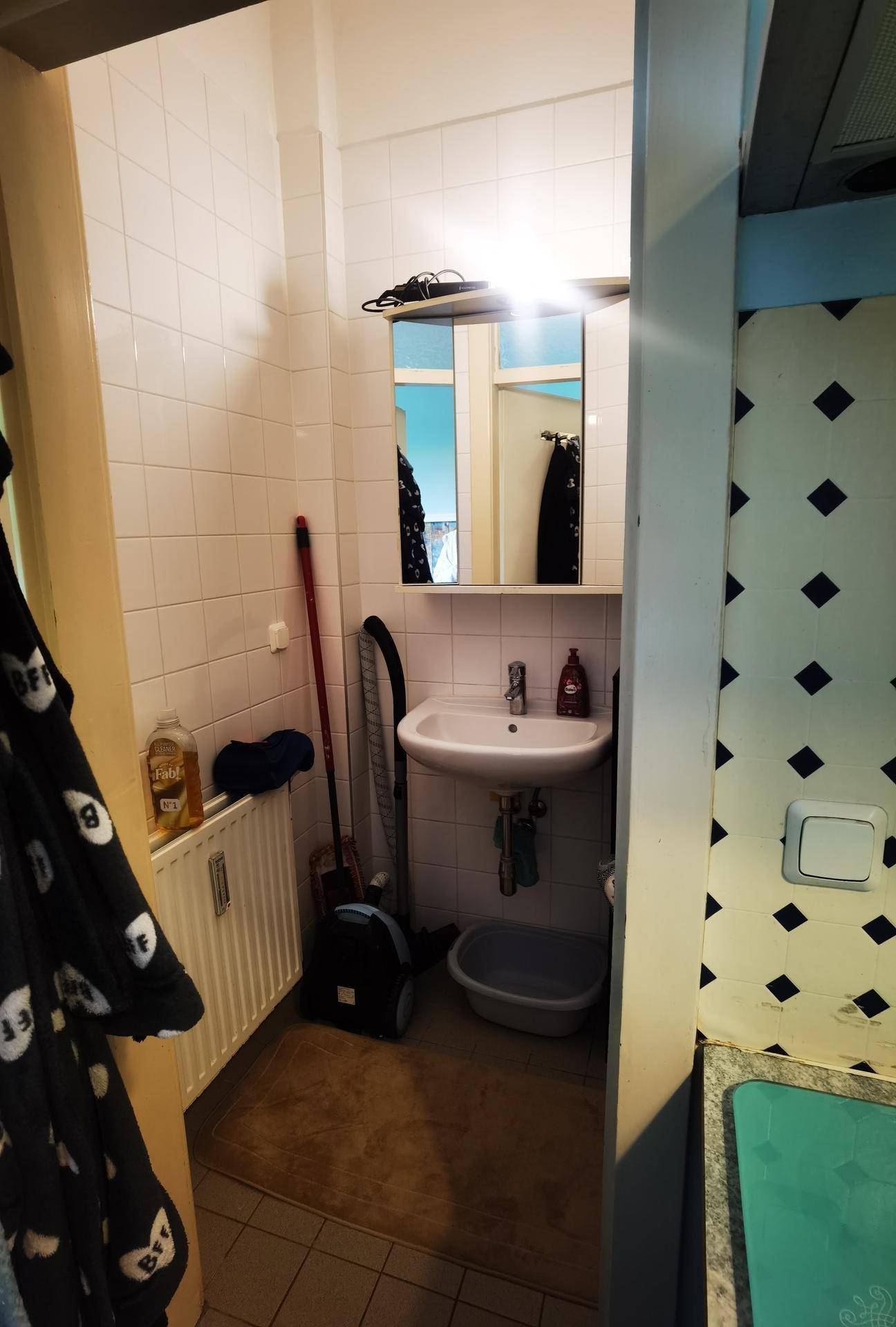 Badezimmer mit Waschbecken, Spiegelschrank, Heizkörper und weiß gefliesten Wänden.