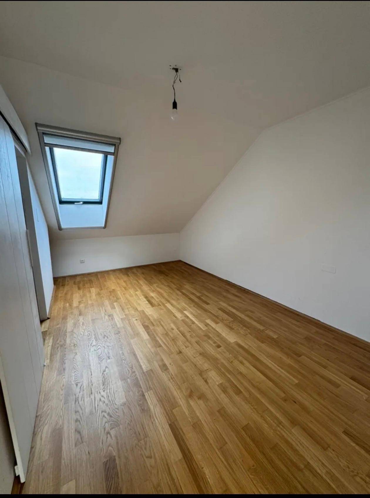 Helles Schlafzimmer mit Parkettboden, weißen Wänden und einem Dachfenster in der Dachschräge.