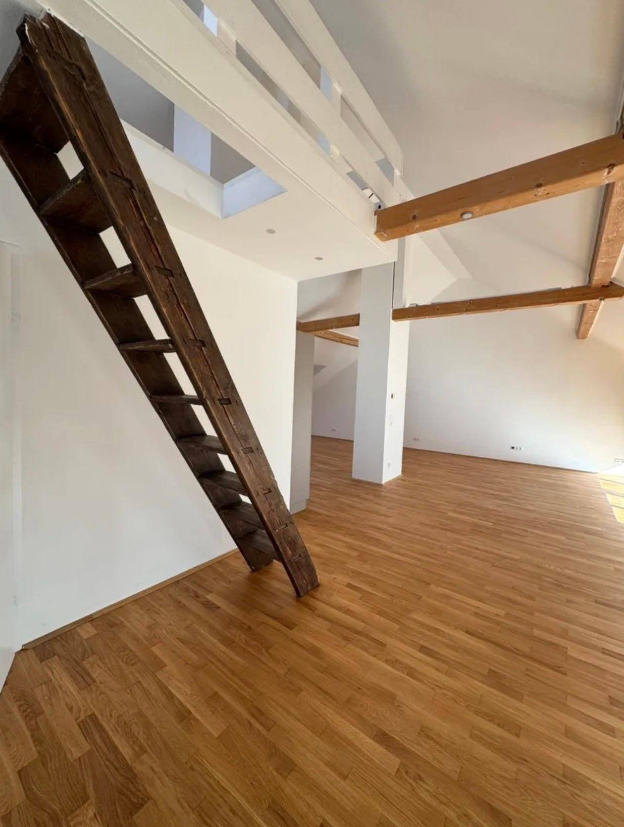 Geräumiger Wohnbereich mit sichtbaren Holzbalken und einer rustikalen Holzleiter, die zu einer oberen Ebene führt.