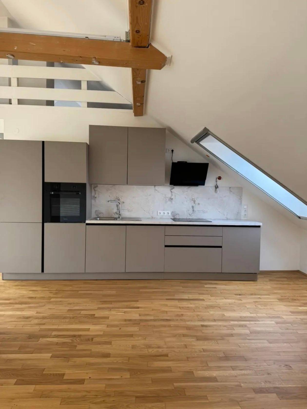 Moderne Küchenzeile in Grau mit integriertem Backofen, Dunstabzugshaube und Marmor-Rückwand unter einem Dachfenster.