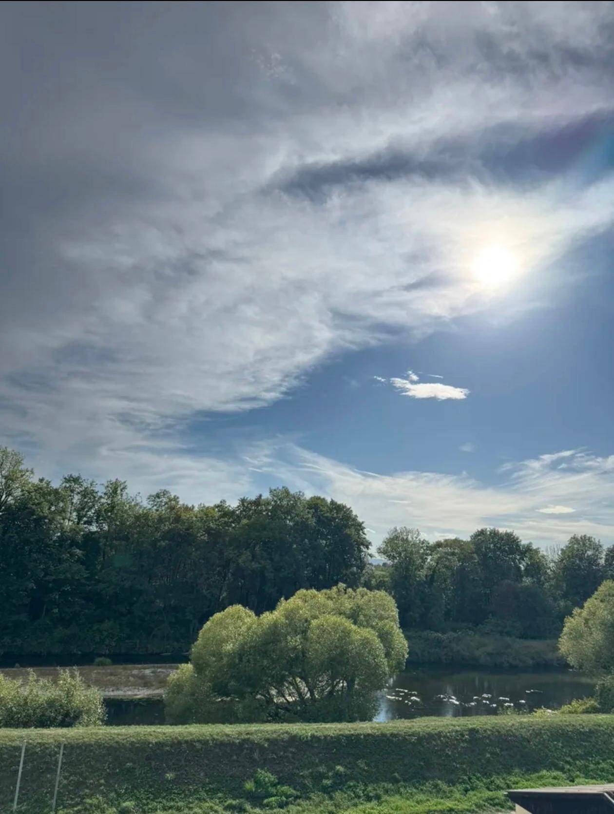 Malerischer Ausblick auf einen Fluss oder See, umgeben von üppiger grüner Natur unter einem weiten Himmel.
