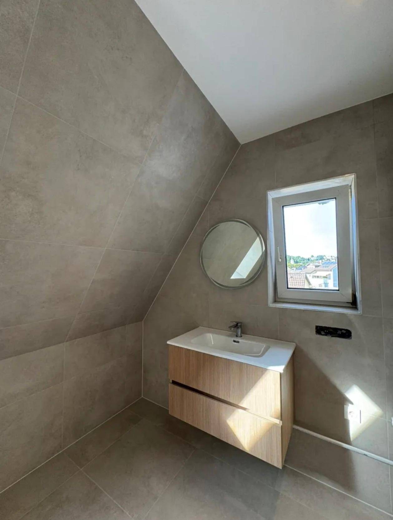 Modernes Badezimmer mit Waschtisch, rundem Spiegel und Fenster, das einen weiten Ausblick bietet.