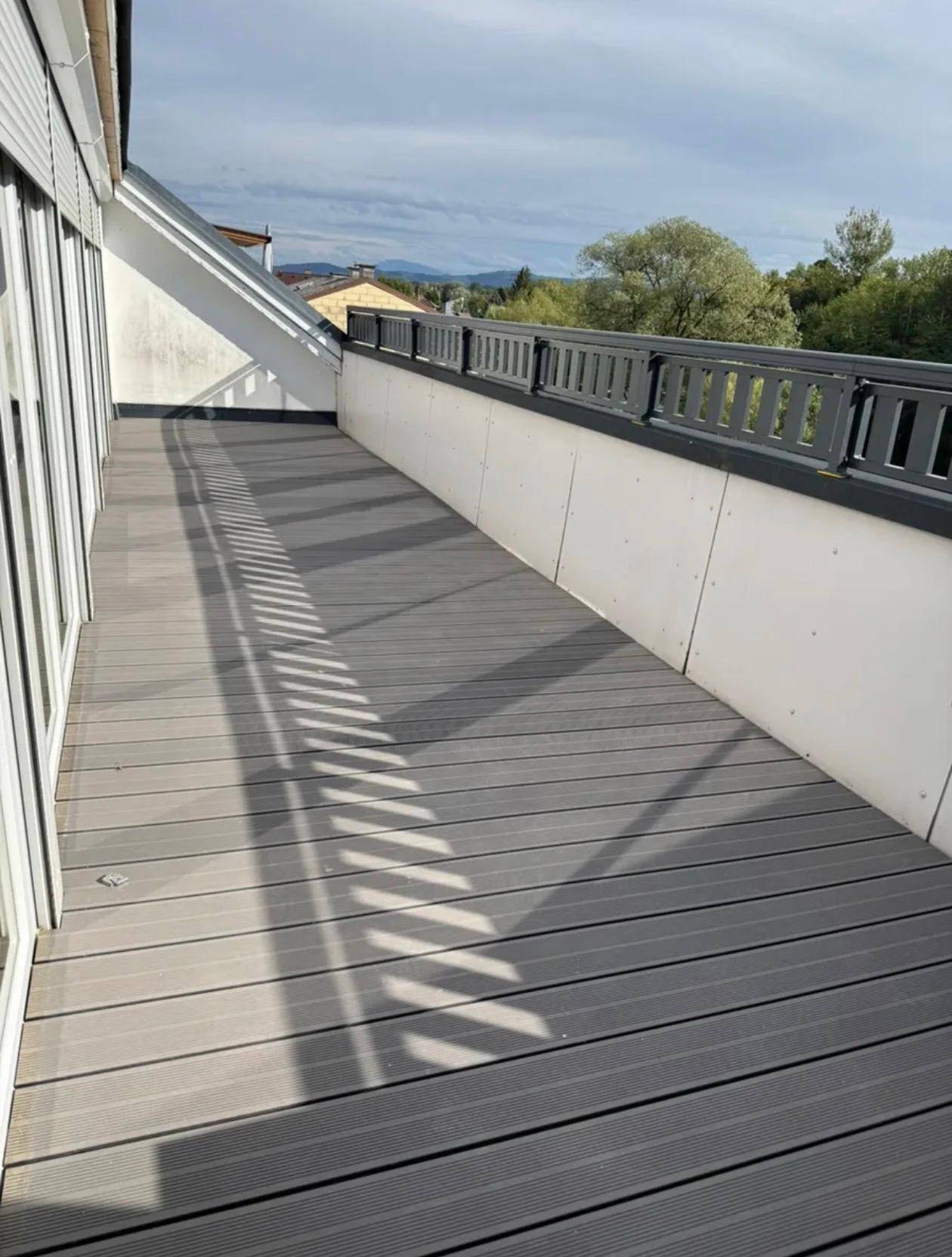 Große Sonnenterrasse mit modernen grauen Dielen und einem stabilen Geländer, ideal für Entspannung im Freien.
