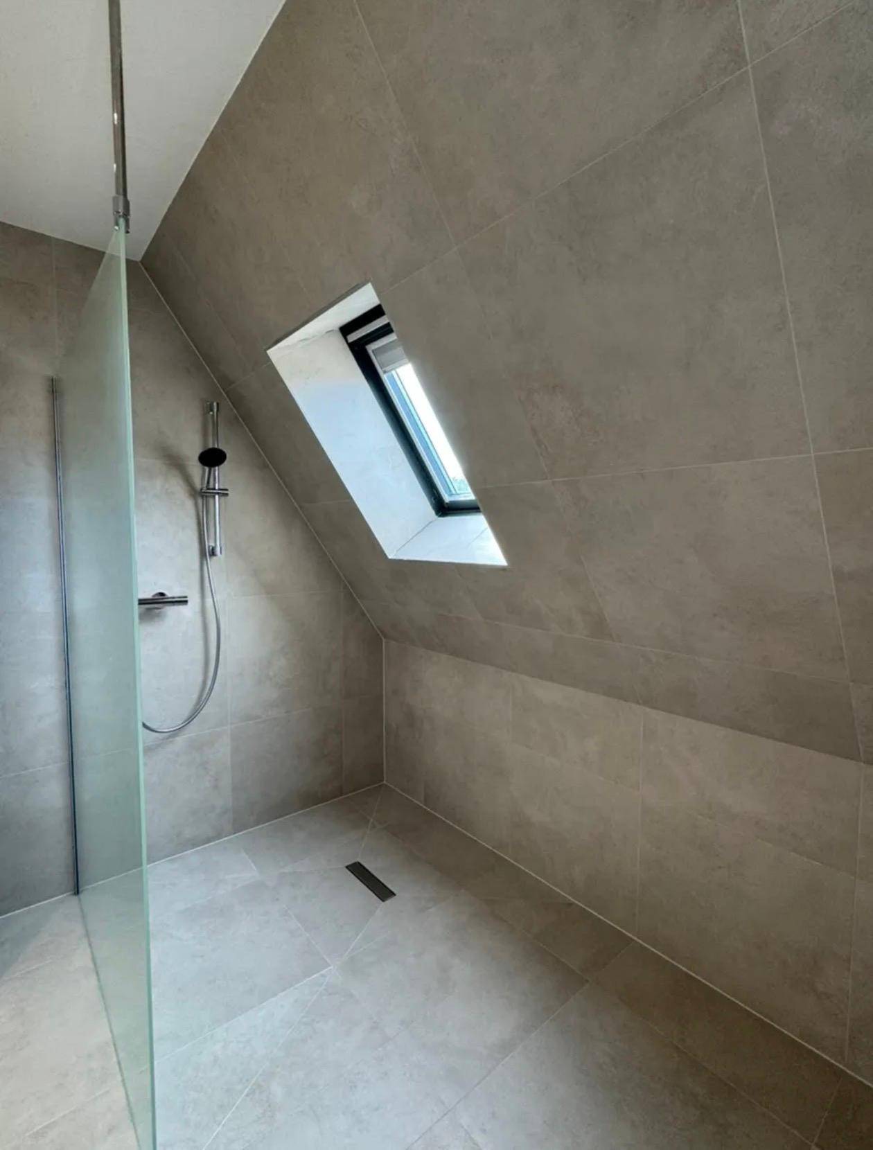 Modernes Badezimmer mit begehbarer Dusche, grauen Fliesen und einem Dachfenster in der Schräge.