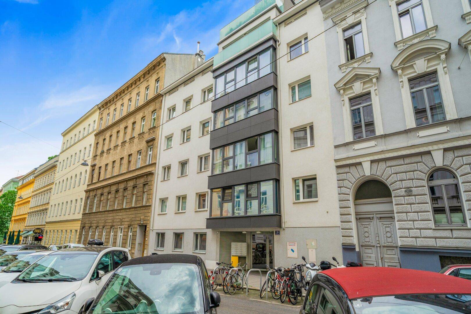 Moderne Wohnhausfassade in einer städtischen Umgebung mit parkenden Autos.