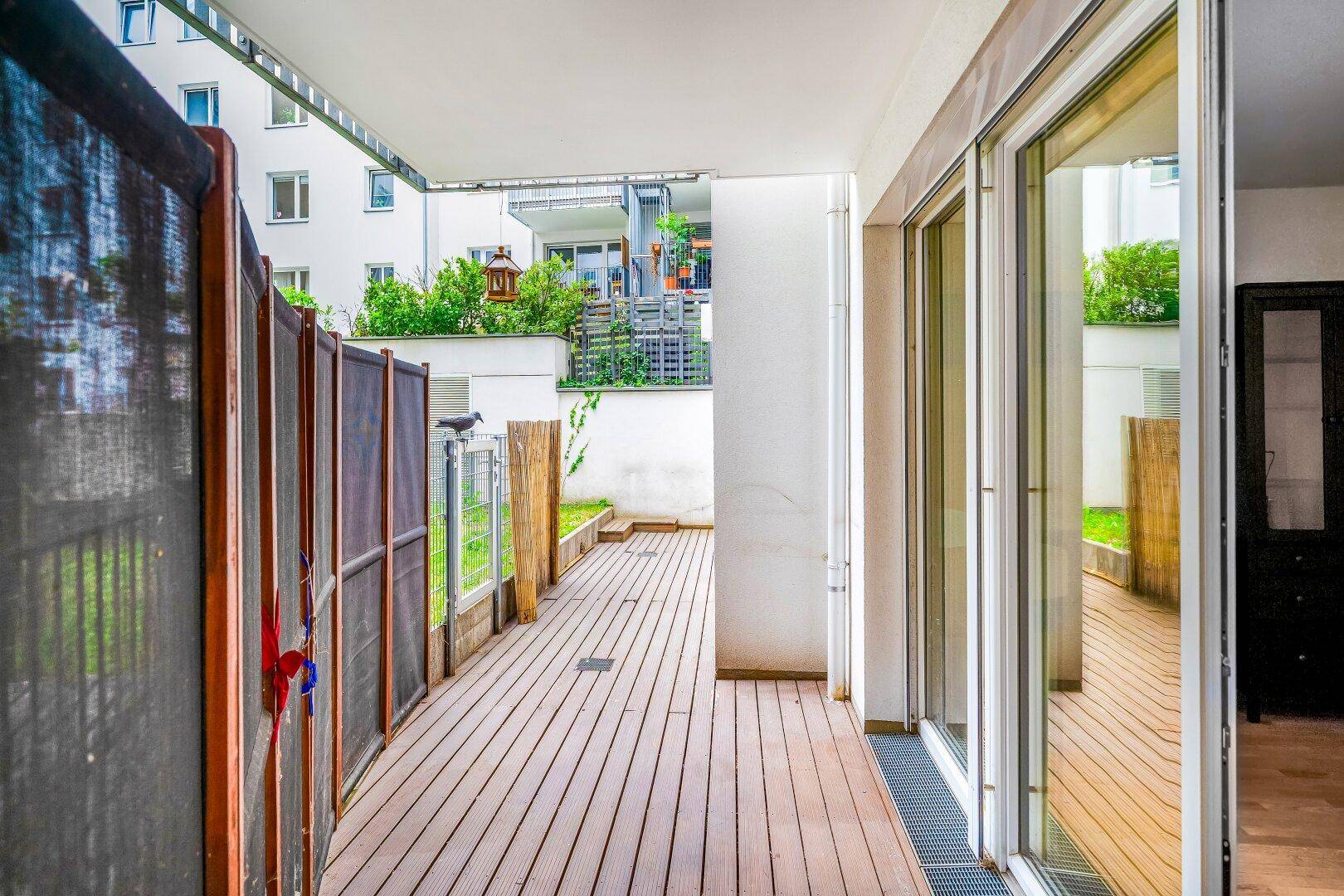 Holzterrasse mit Sichtschutz und Blick auf den Innenhof des Gebäudes.
