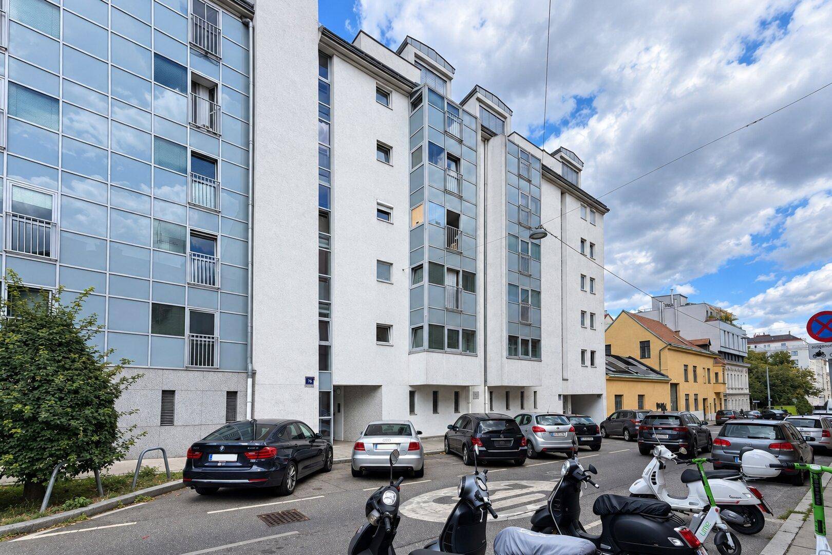 Moderne Wohngebäude-Fassade mit Glasfronten und Parkplätzen an der Straße.