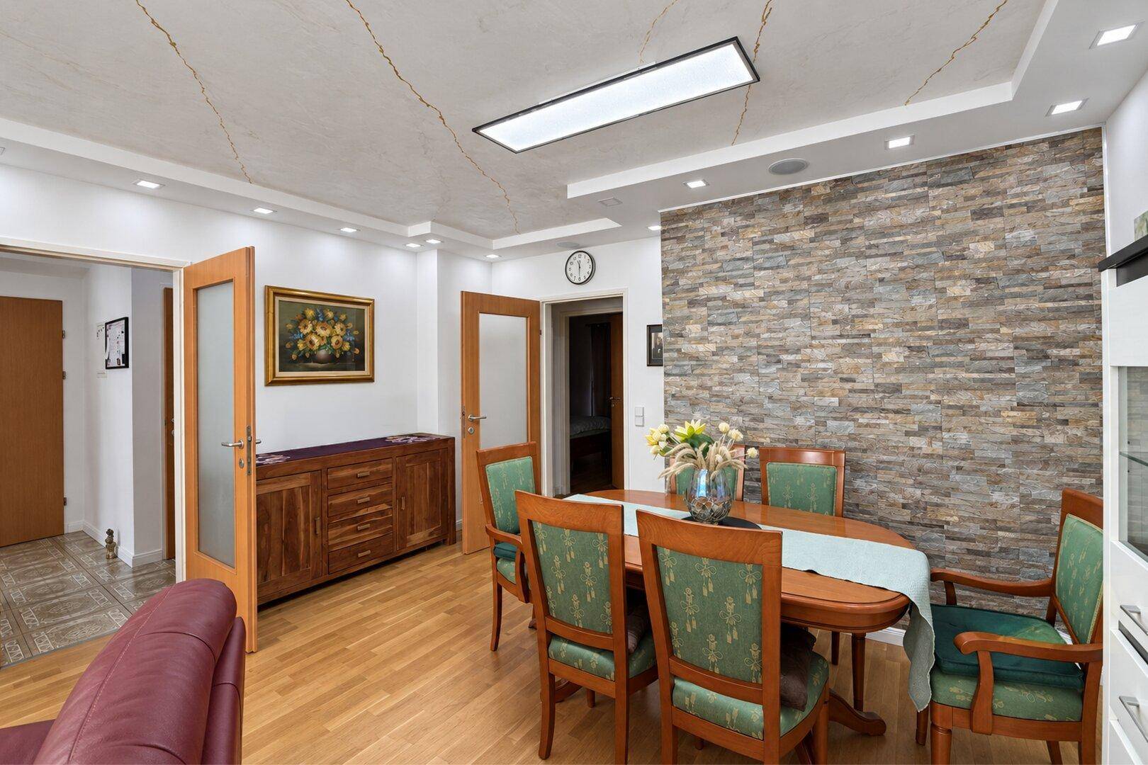 Essbereich mit Holztisch und Stühlen, akzentuiert durch eine moderne Steinwand und Holzboden.