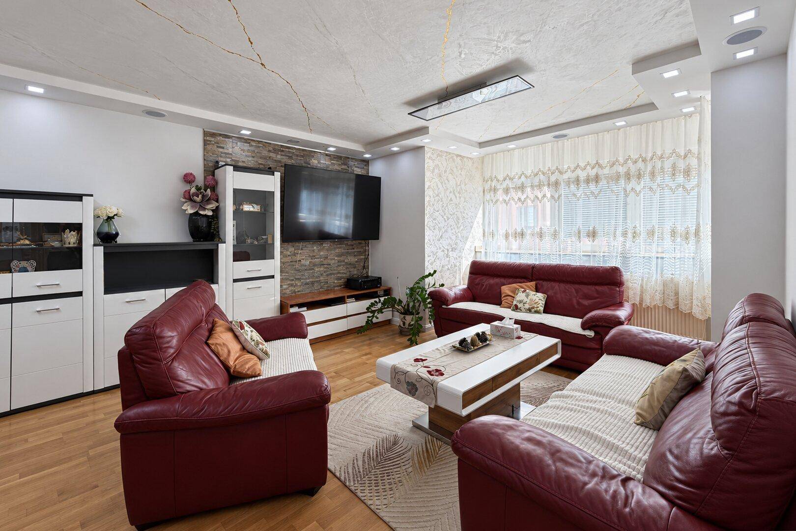 Gemütliches Wohnzimmer mit roten Ledersofas, Couchtisch und Fernseher an der Wand.