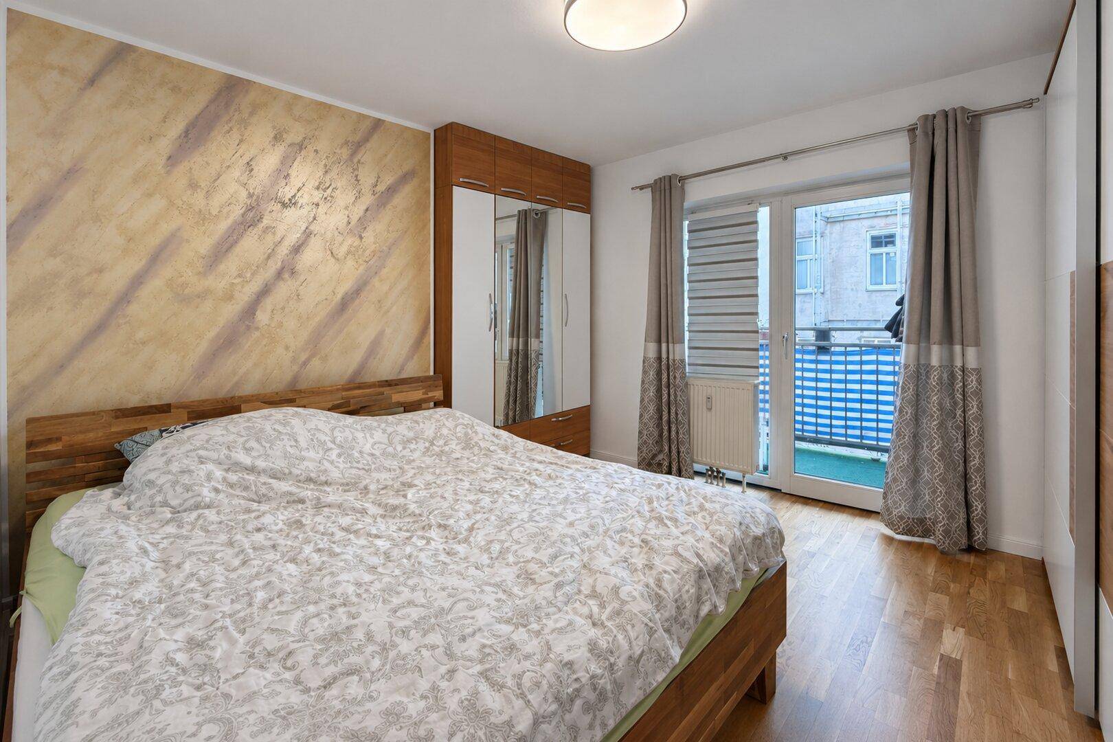 Schlafzimmer mit Doppelbett, Spiegelschrank und direktem Zugang zu einem kleinen Balkon.
