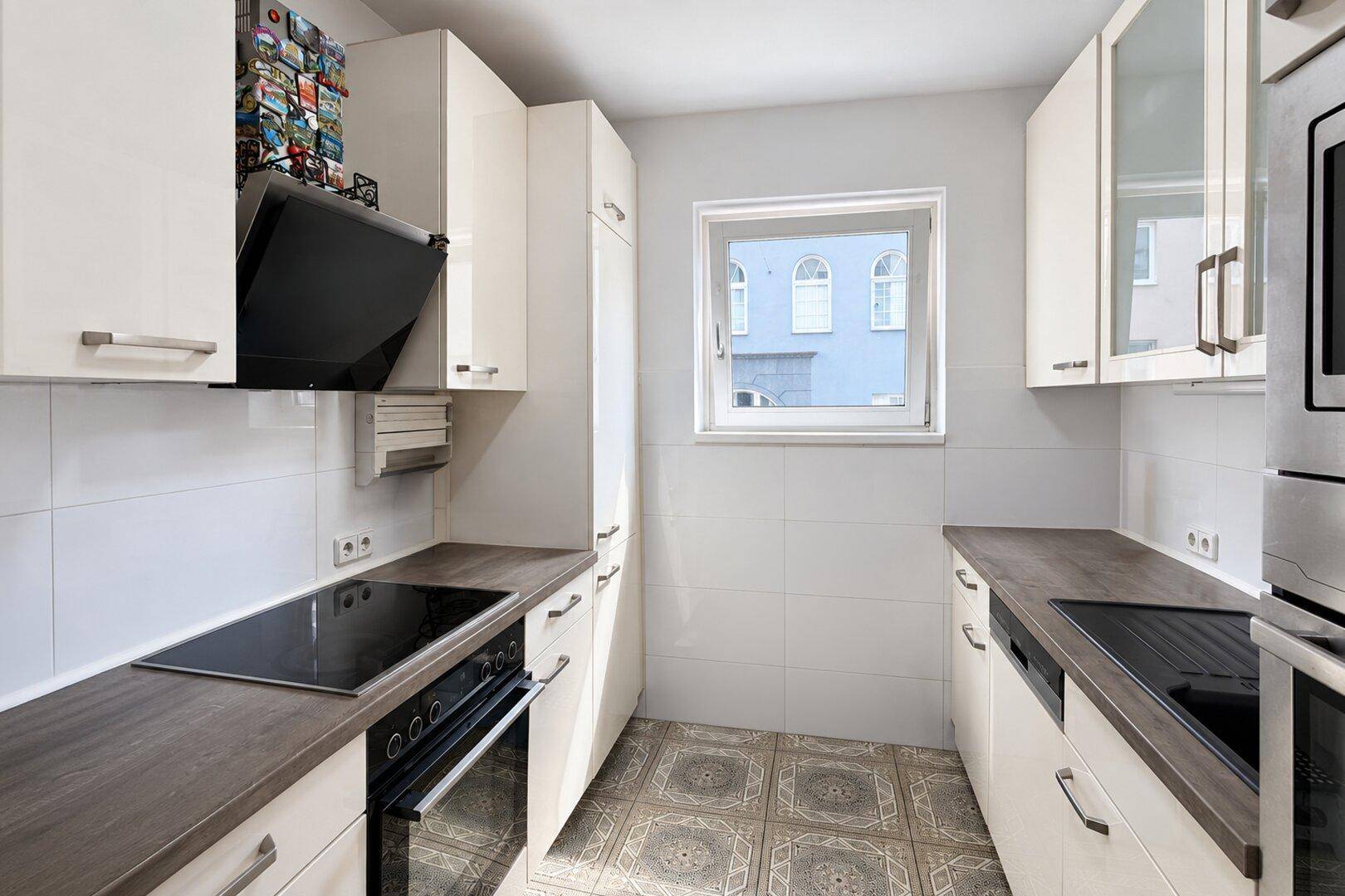 Kleine Küche mit weißen Schränken, Induktionskochfeld, Backofen und Fenster.