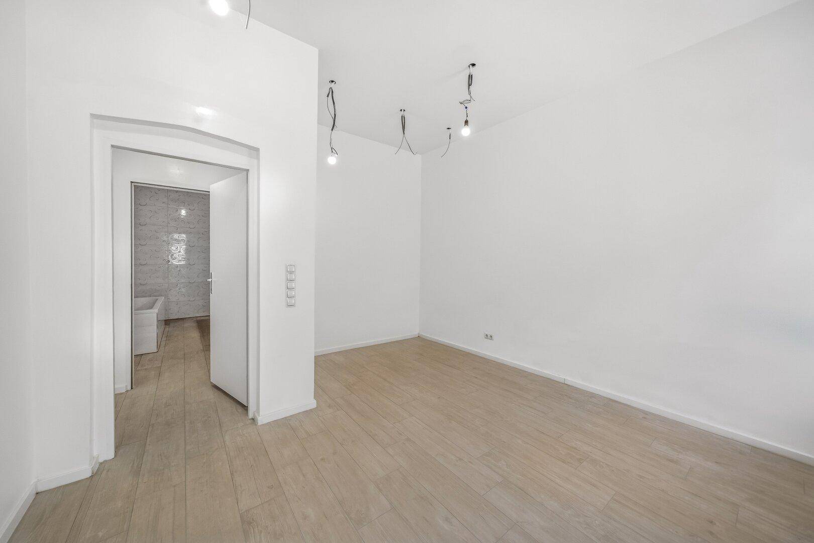 Heller, leerer Raum mit Zugang zu einem angrenzenden Badezimmer und Holzboden.