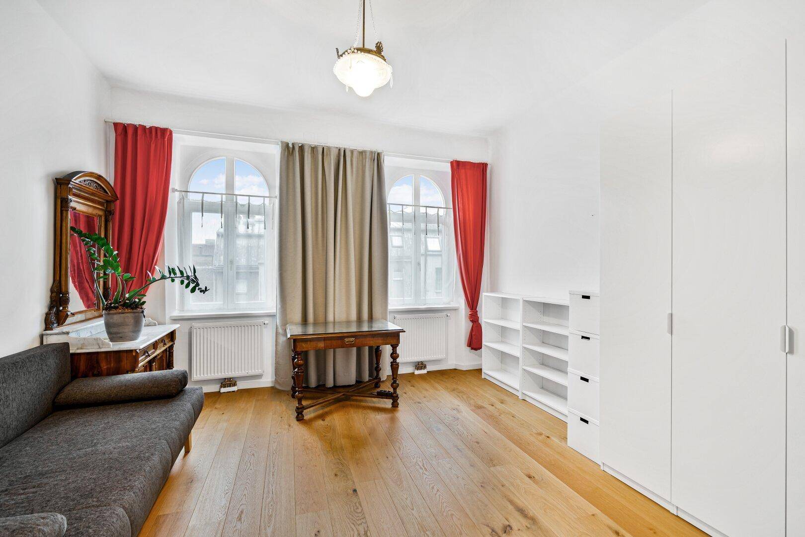 Helles Wohnzimmer mit Sofa, weißen Schränken und Regalen, sowie Parkettboden.