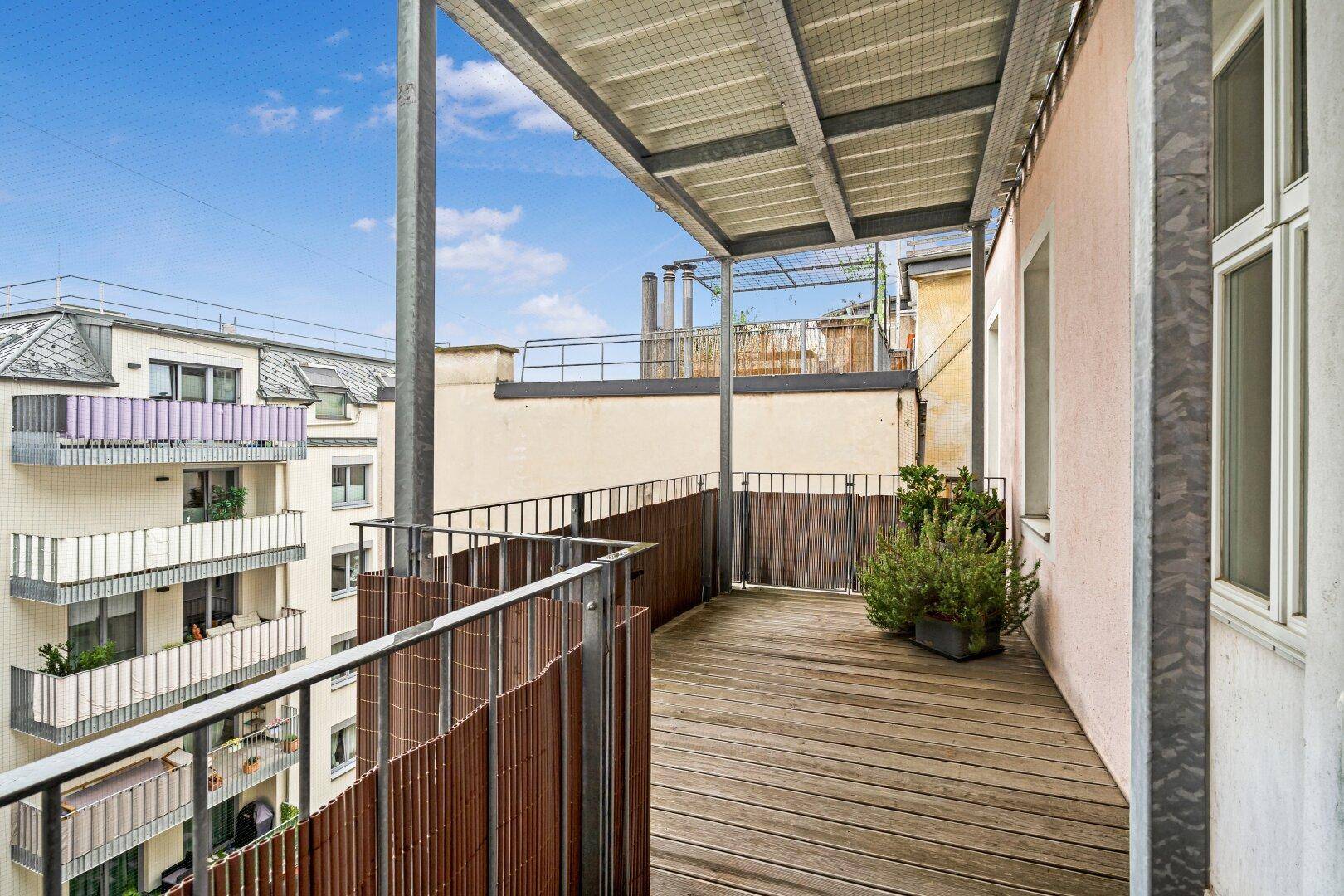 Geräumiger Balkon mit Holzbelag und Metallgeländer, bietet Blick auf die Umgebung.