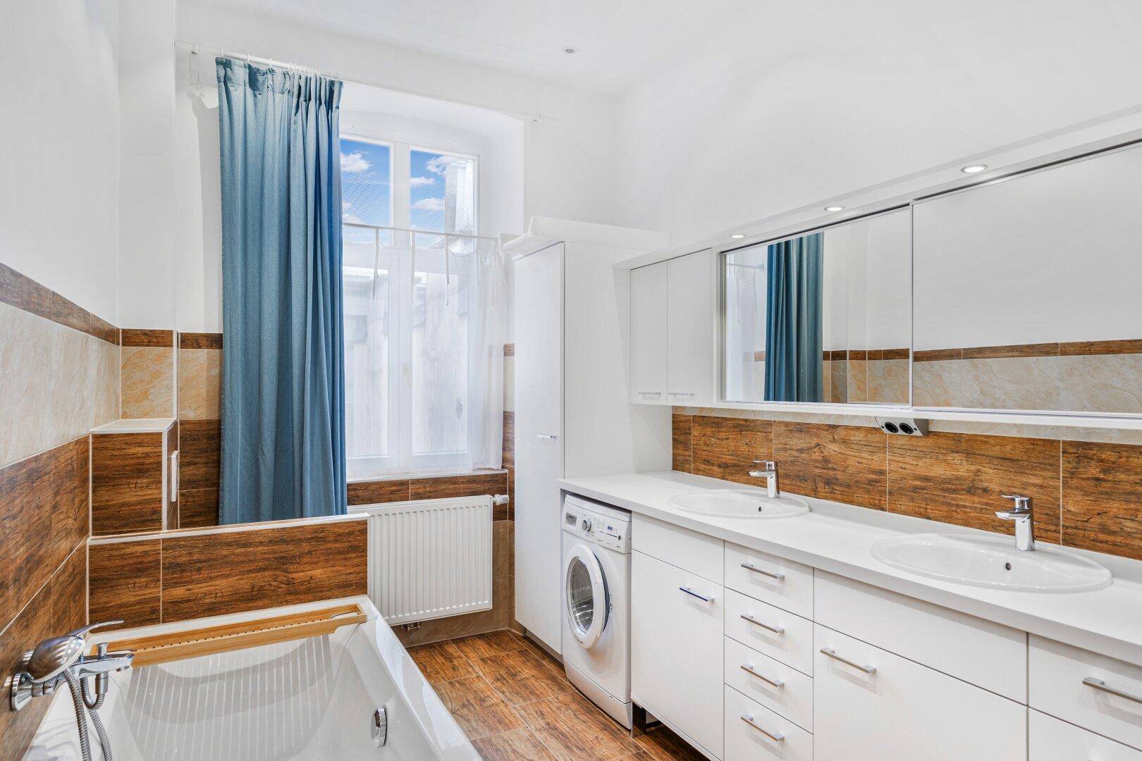Modernes Badezimmer mit Badewanne, Doppelwaschbecken und Waschmaschine am Fenster.