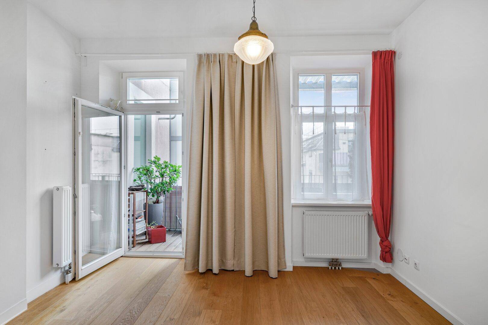 Heller Raum mit Parkettboden und Zugang zu einem Balkon durch eine Glastür.