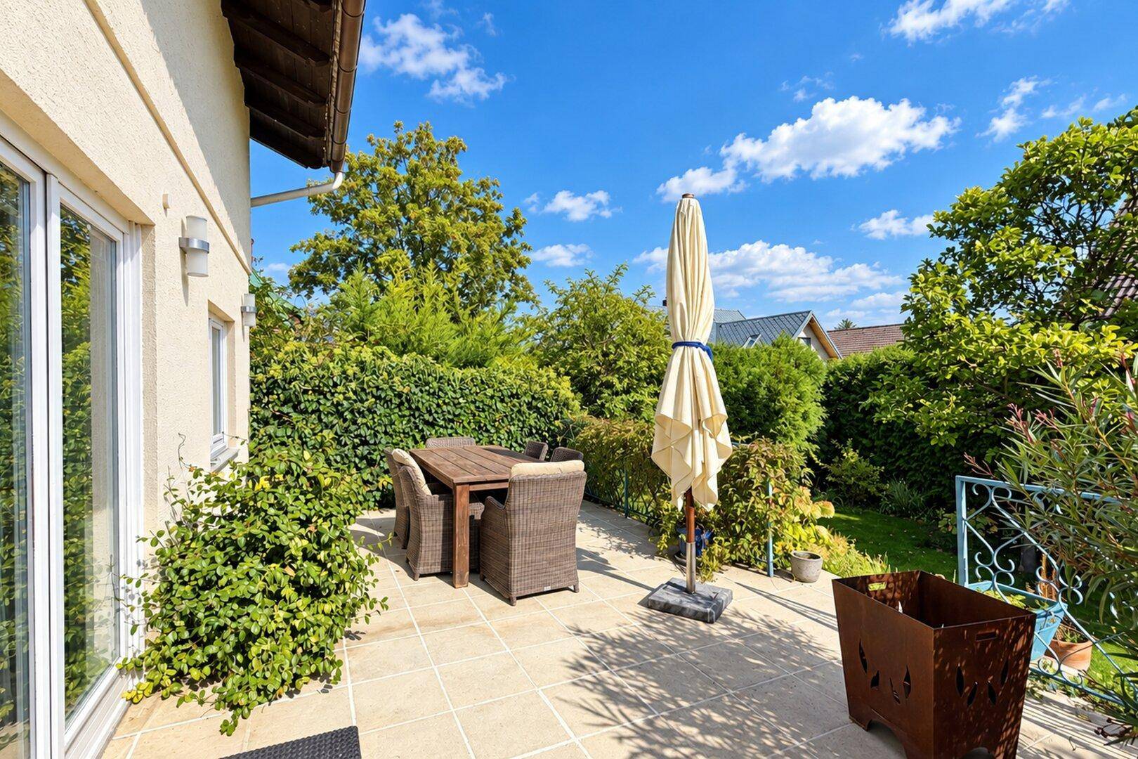 Sonnige Terrasse mit Gartenmöbeln, großem Sonnenschirm und Blick ins Grüne.