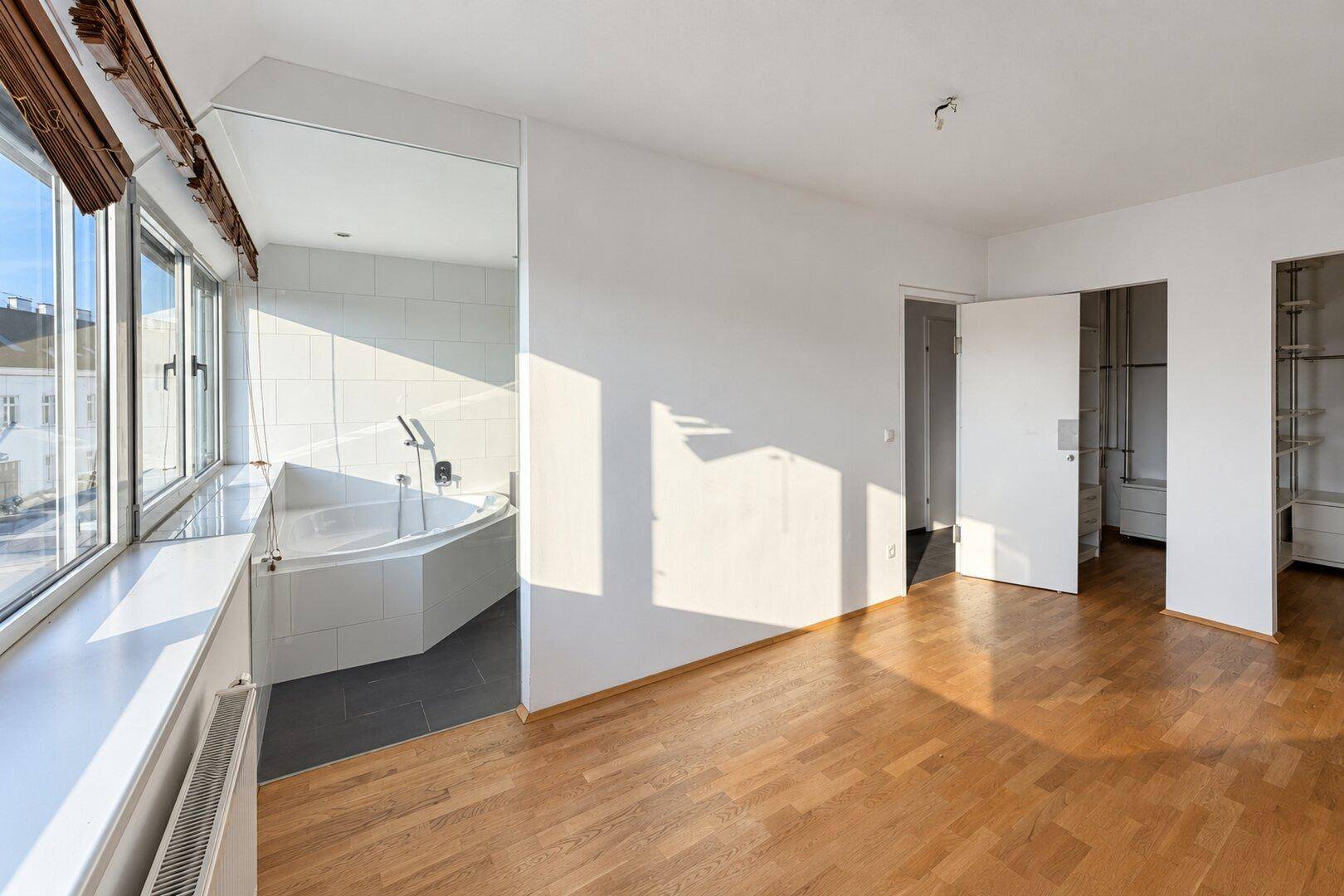Helles Schlafzimmer mit Holzboden und integriertem Badezimmerbereich mit Eckbadewanne.