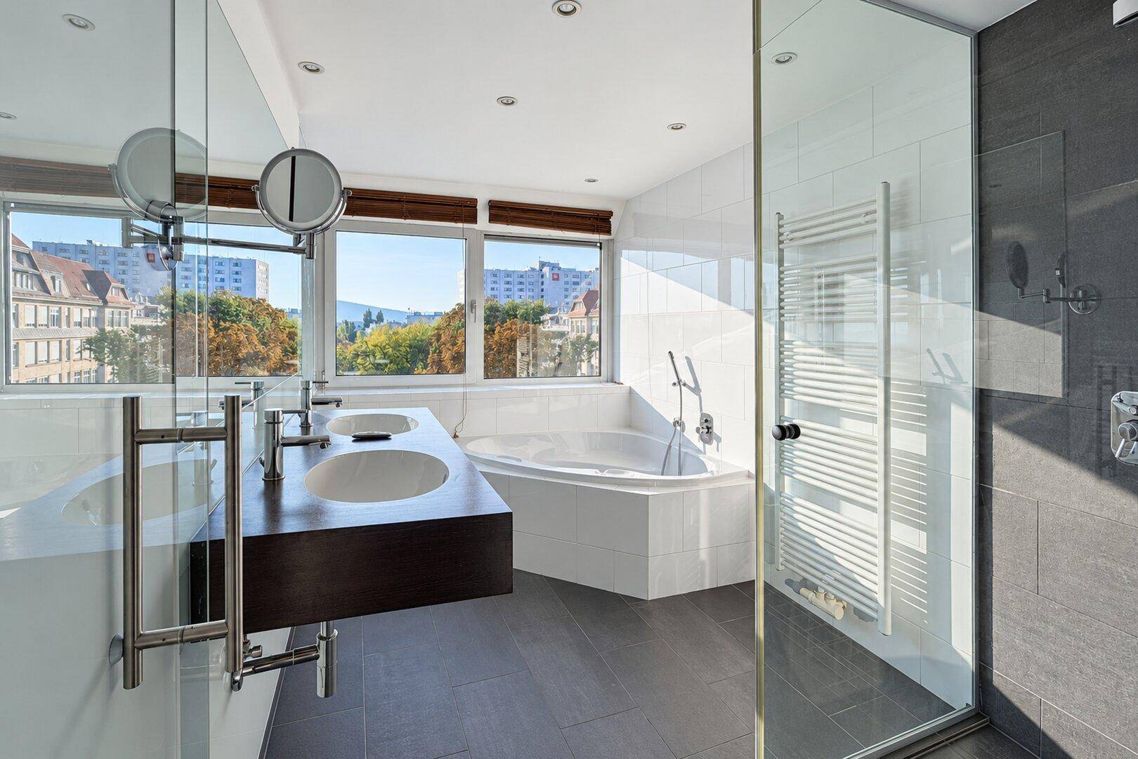 Modernes Badezimmer mit Doppelwaschbecken, Eckbadewanne, begehbarer Dusche und Fenster mit Ausblick.