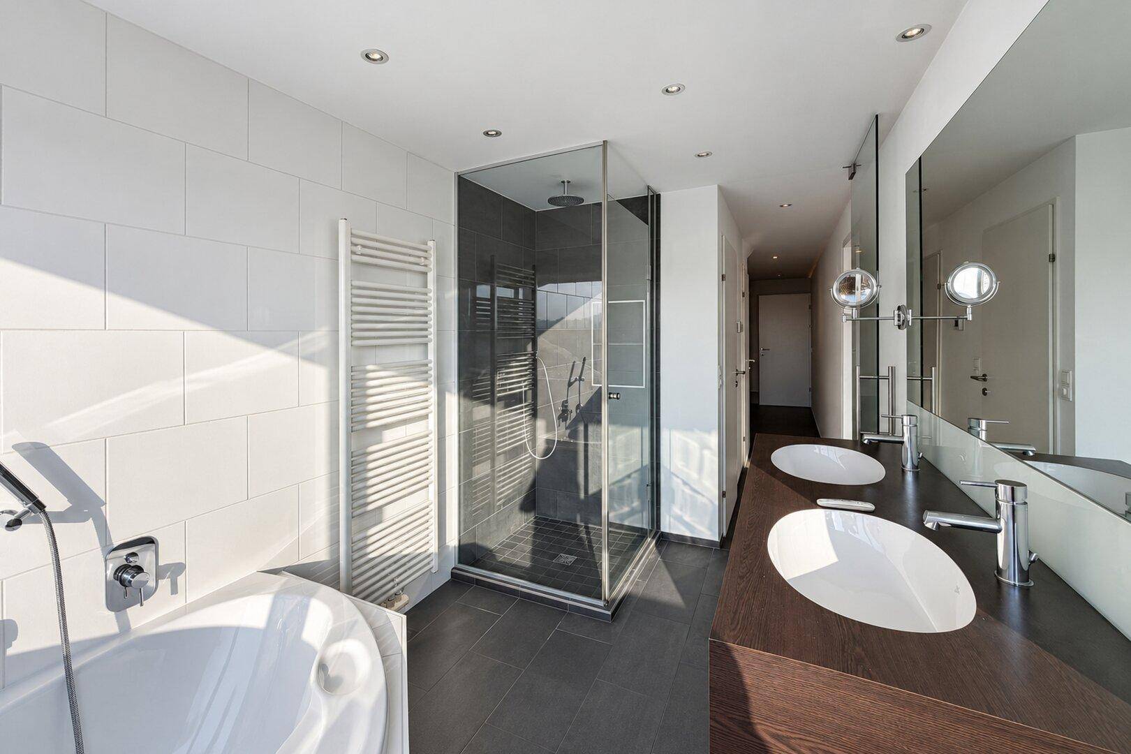 Elegantes Badezimmer mit Doppelwaschbecken, großer Duschkabine und moderner Eckbadewanne.