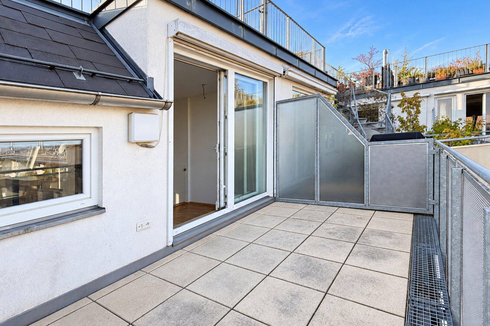 Geräumige Terrasse mit Fliesenboden und Zugang zum Innenbereich, umgeben von Metallgeländern.