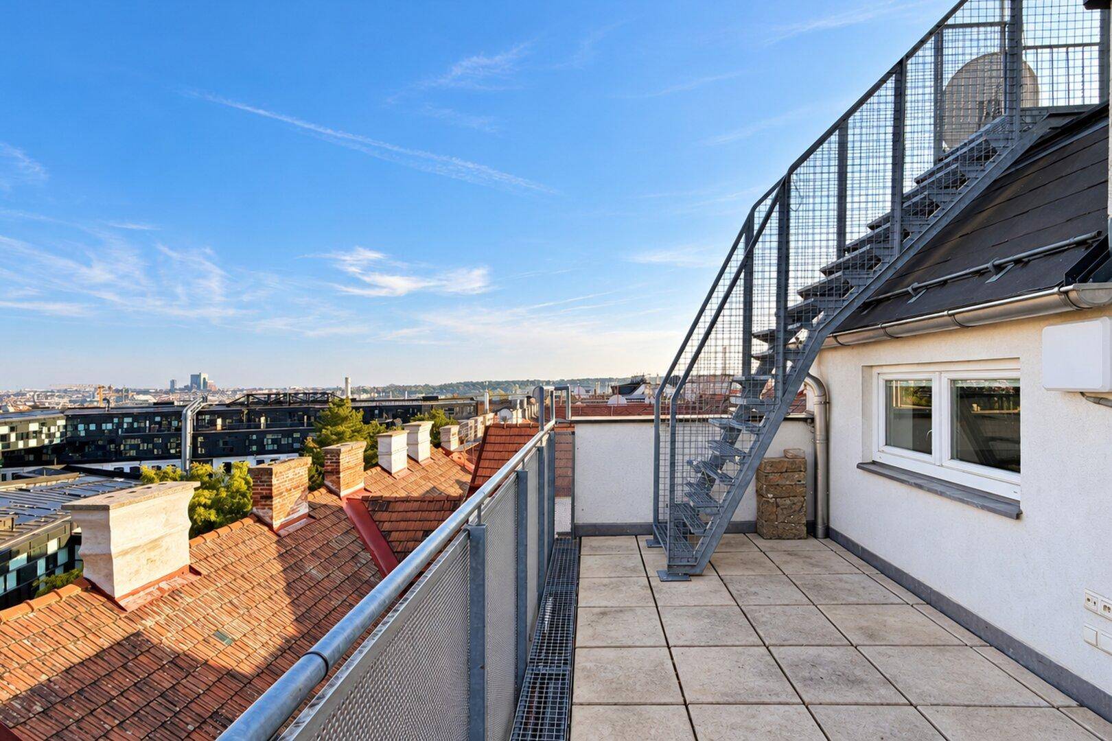 Dachterrasse mit Metalltreppe zum oberen Bereich und weitem Blick über die Dächer der Stadt.