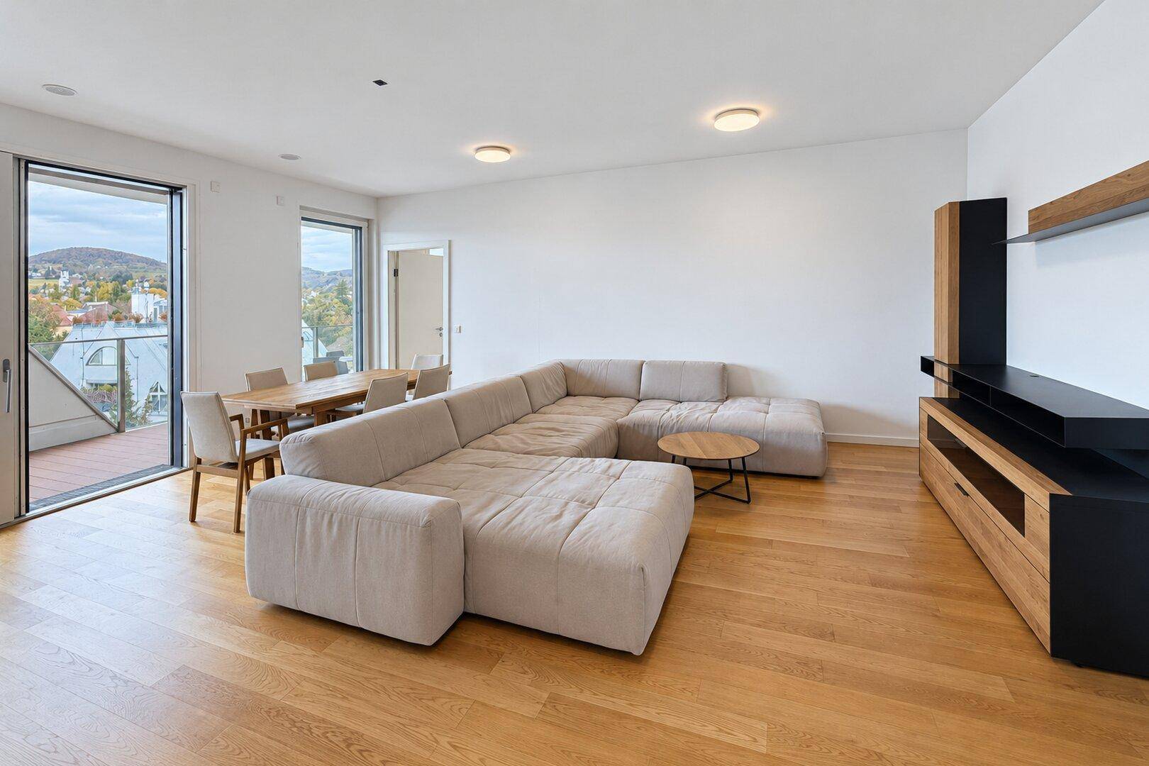 Heller offener Wohn-Essbereich mit Parkettboden, großem Sofa und Zugang zum Balkon.