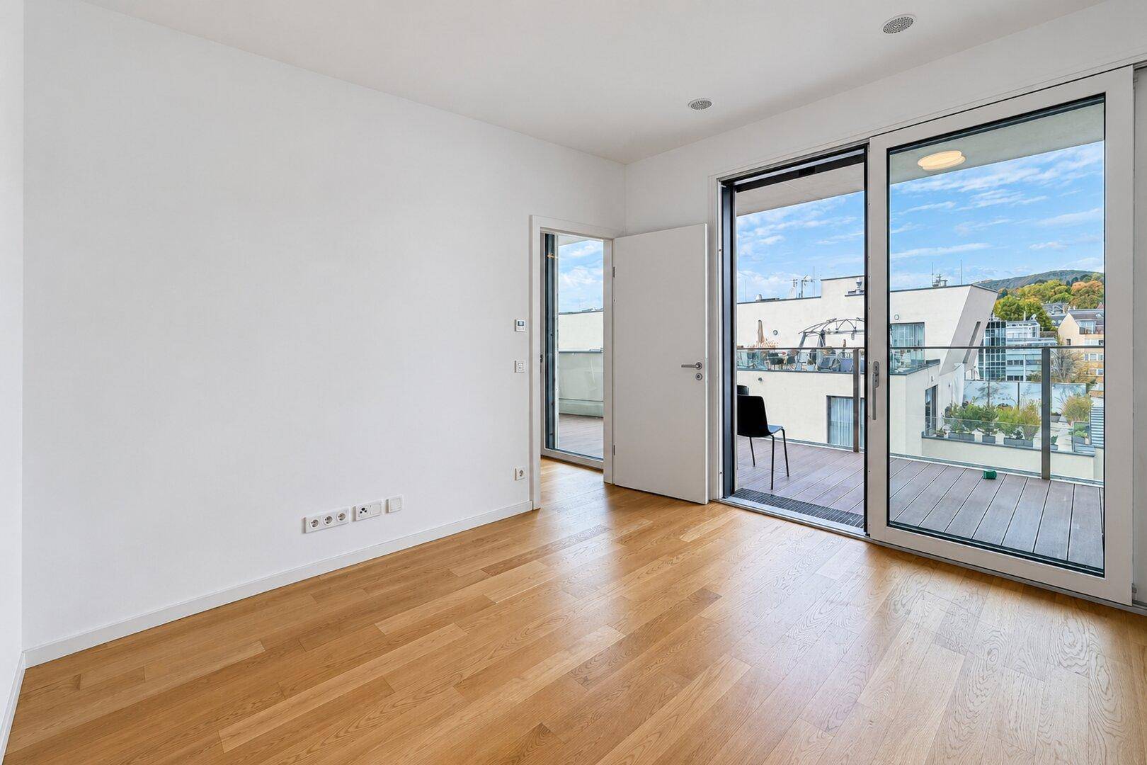 Helles Schlafzimmer mit Parkettboden und Zugang zu einer großen Außenterrasse.