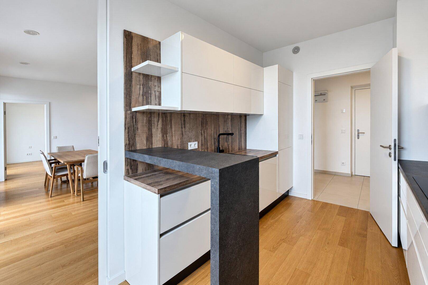 Moderne Küchenzeile mit weißen Schränken, Holzdetails und integrierter Frühstücksbar.