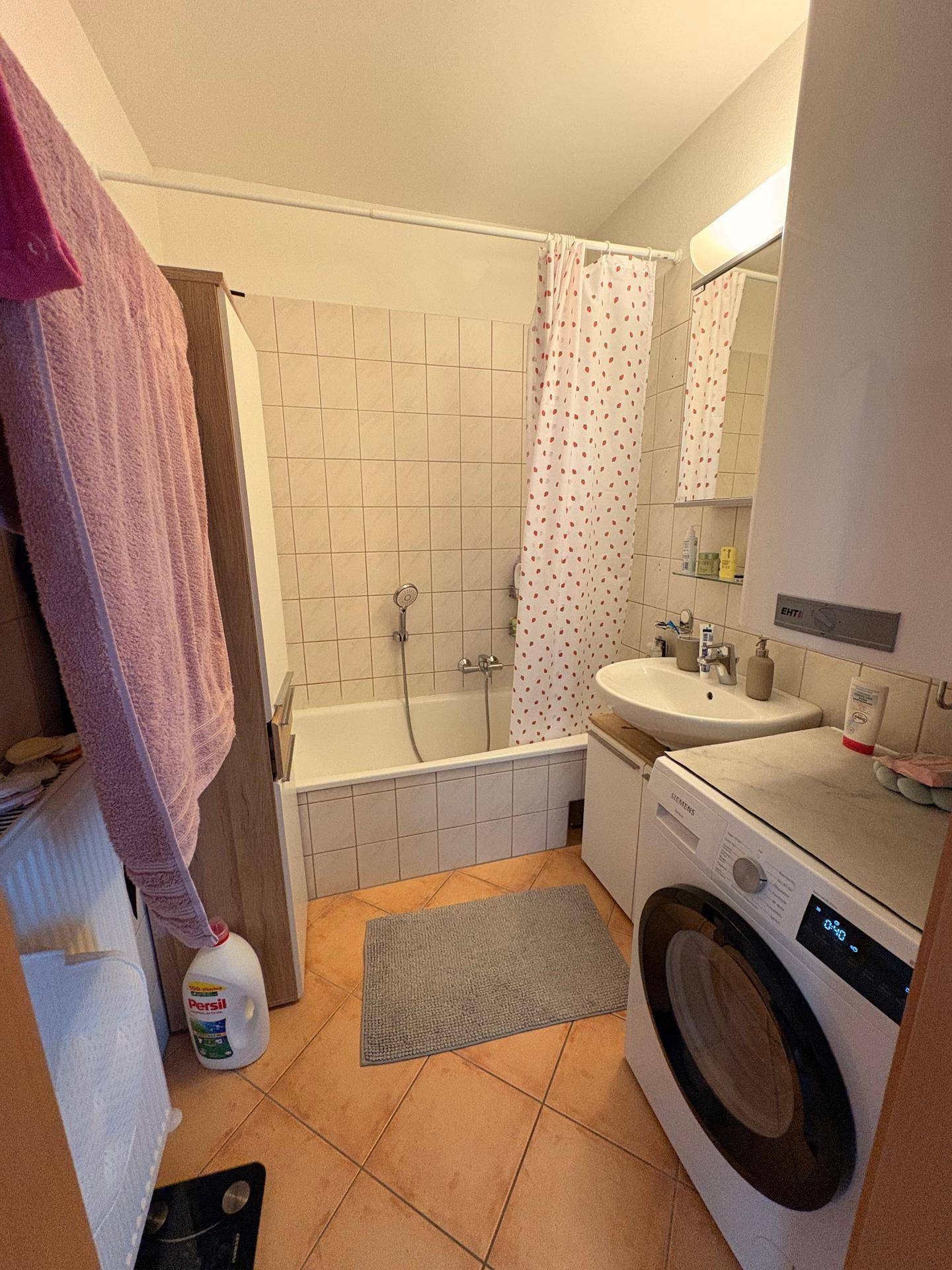 Badezimmer mit Badewanne, Waschbecken, Waschmaschine und Terrakotta-Fliesenboden.