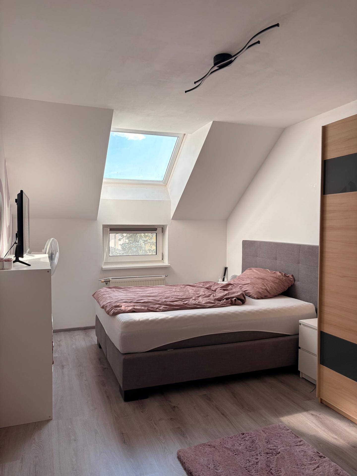 Schlafzimmer mit Bett, Dachfenster, Kleiderschrank und schrägen Wänden.