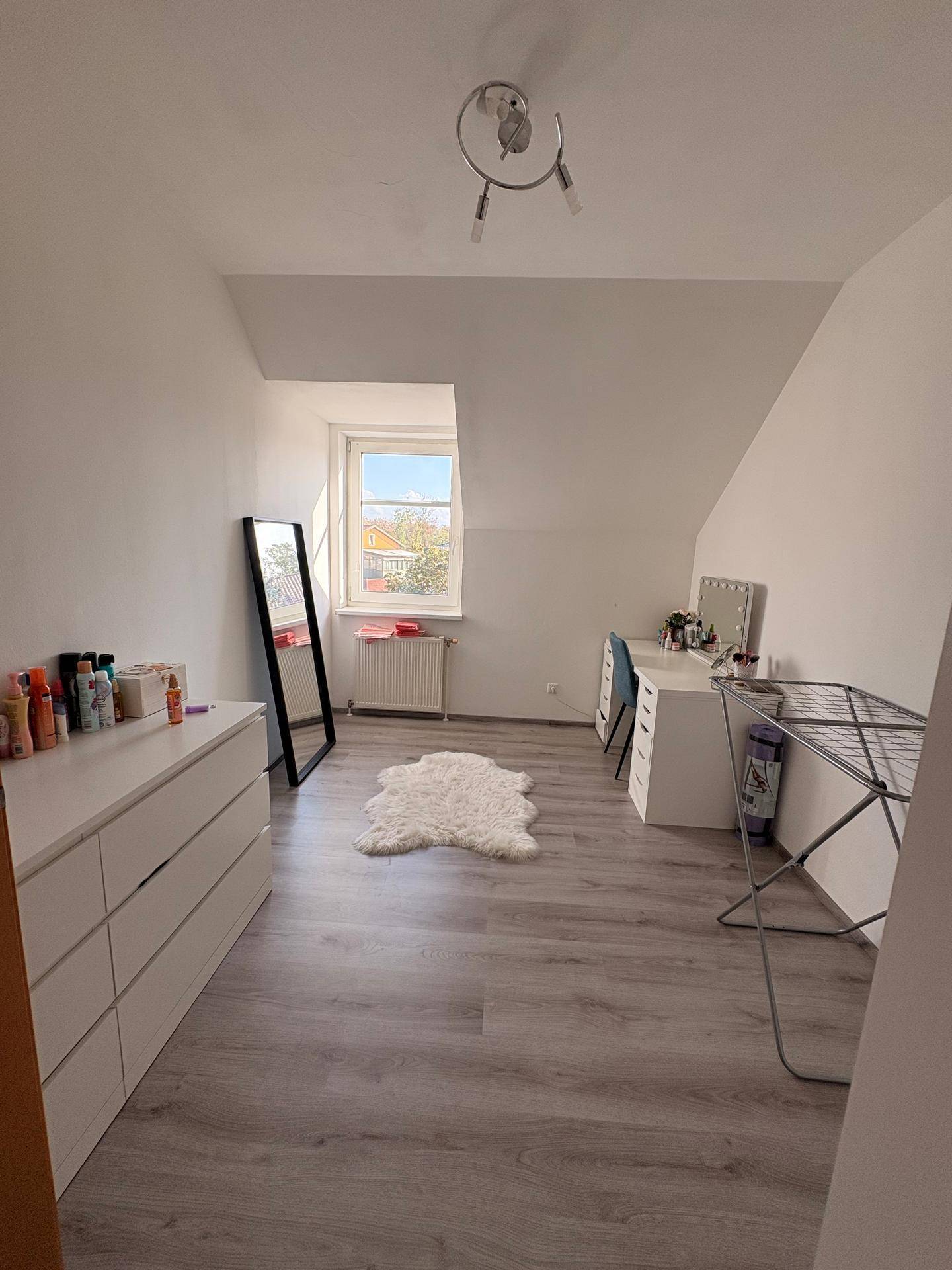 Helles Zimmer mit Schreibtisch, Kommode, Spiegel und Dachschräge.