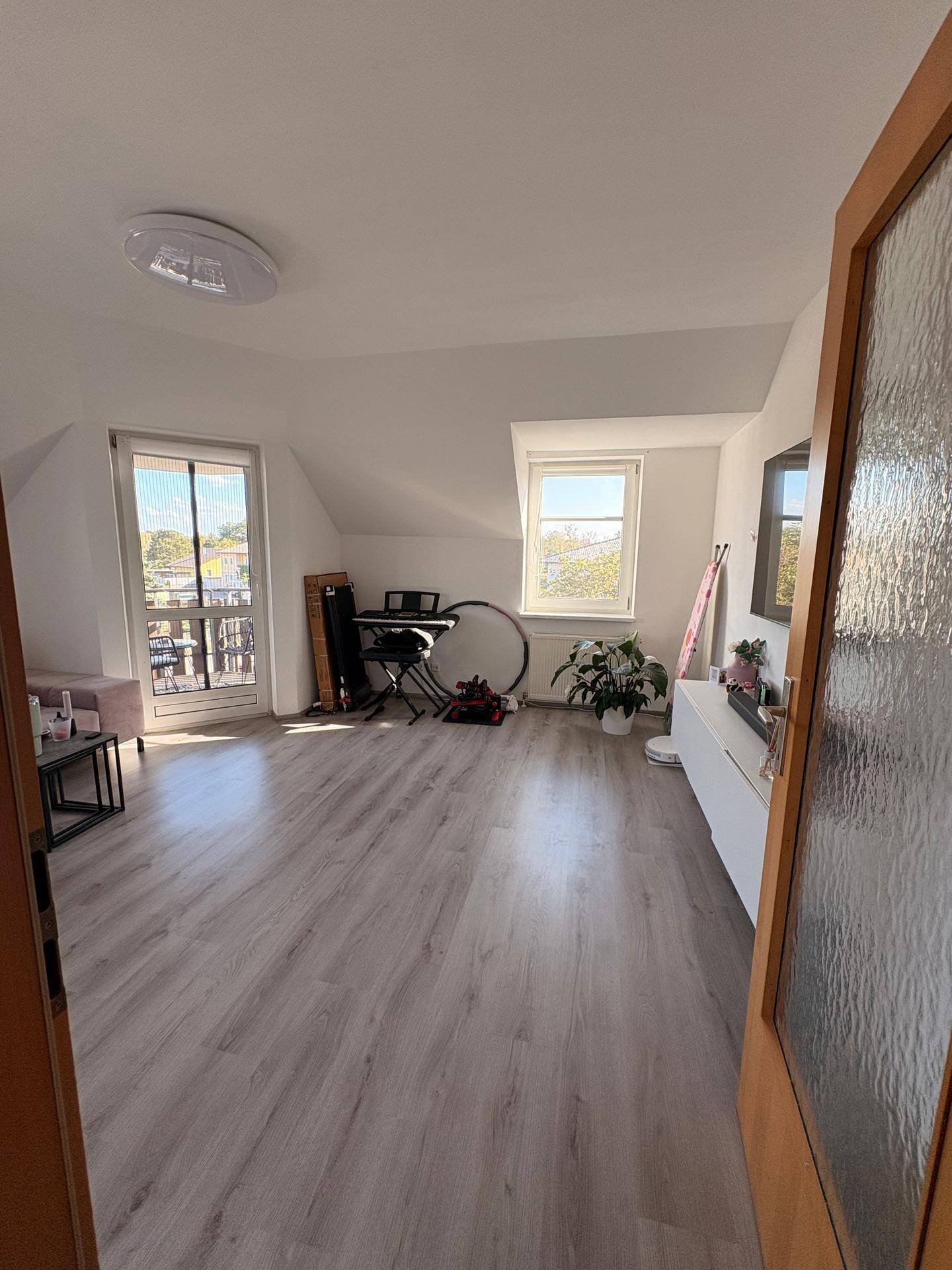 Geräumiges Wohnzimmer mit viel Tageslicht, Laminatboden und Blick nach draußen.