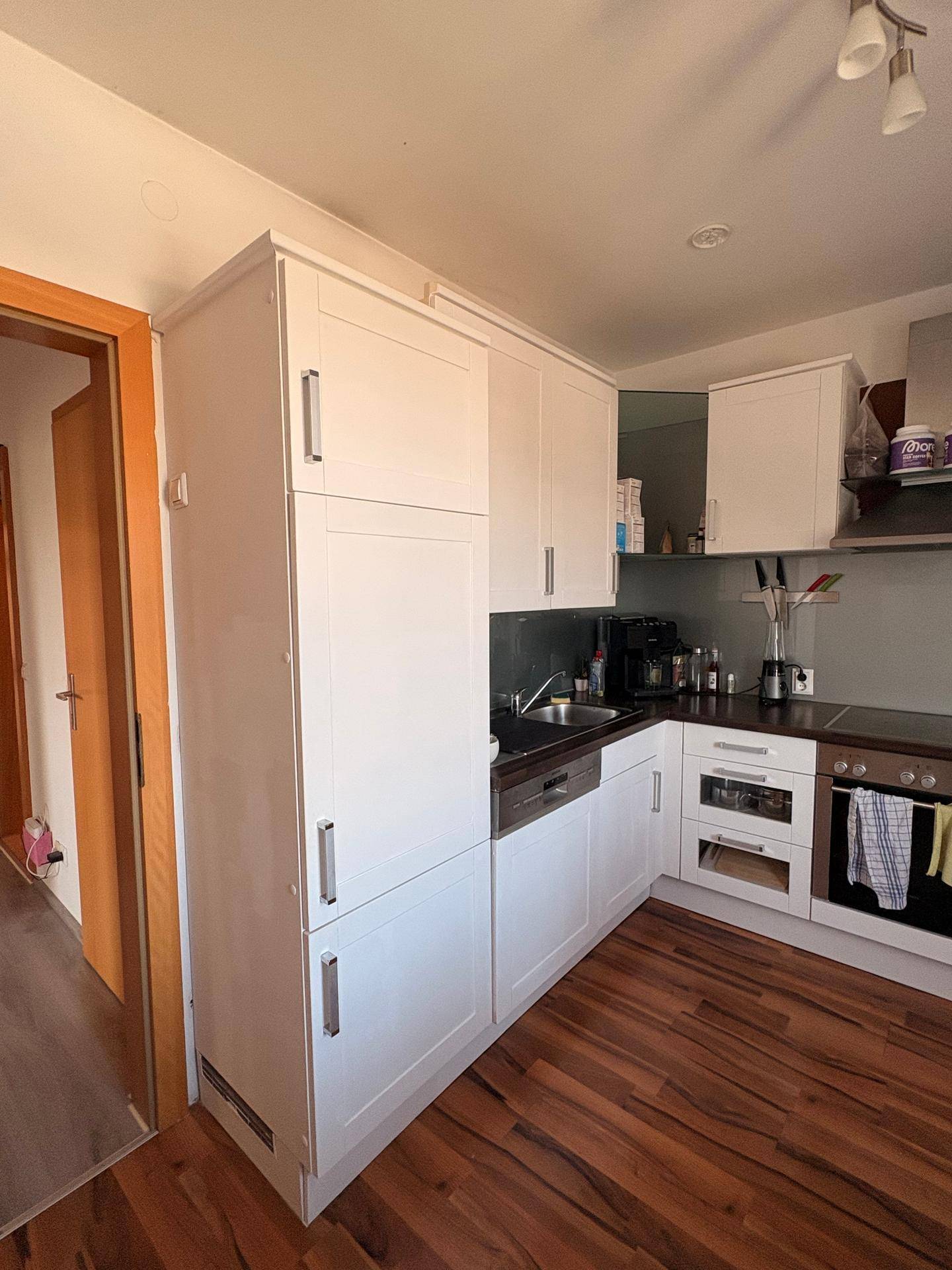 Einbauküche mit weißen Schränken, dunkler Arbeitsplatte und Holzboden.