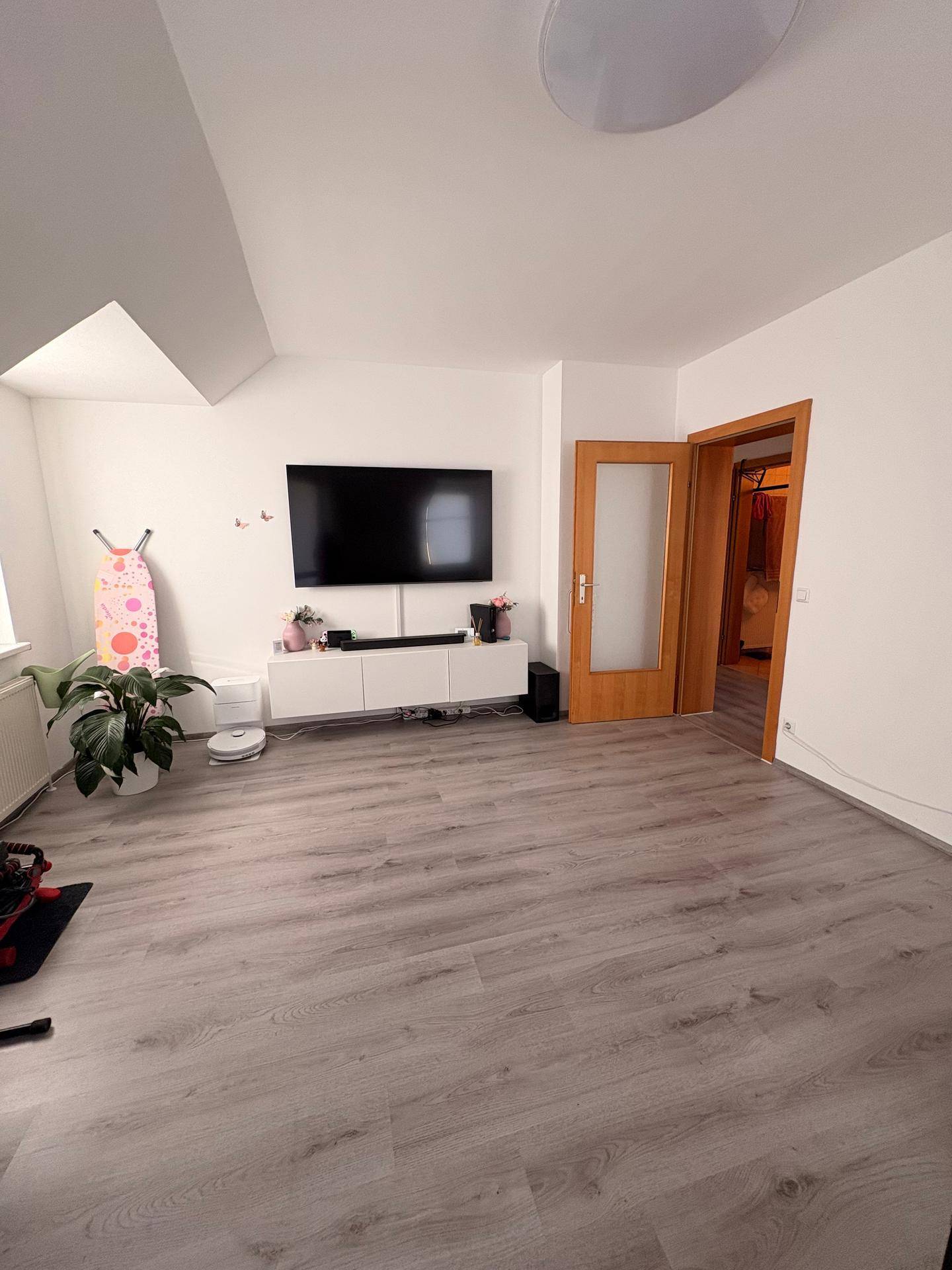 Wohnzimmer mit Wandfernseher, modernem Sideboard und Zugang zu weiteren Räumen.