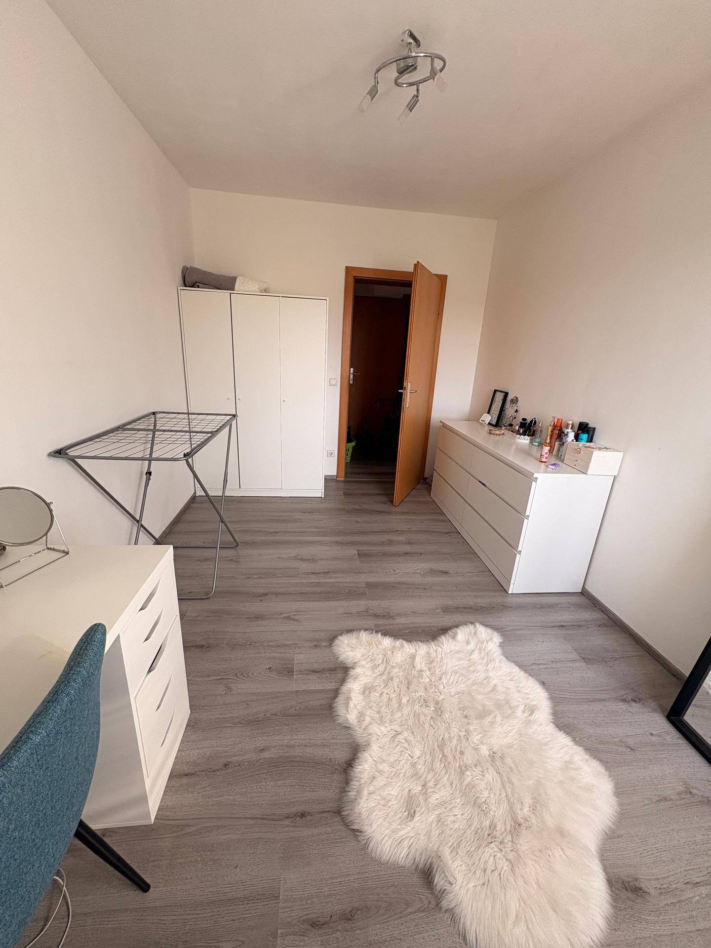 Geräumiges Zimmer mit Laminatboden, Kommode und Wäscheständer.