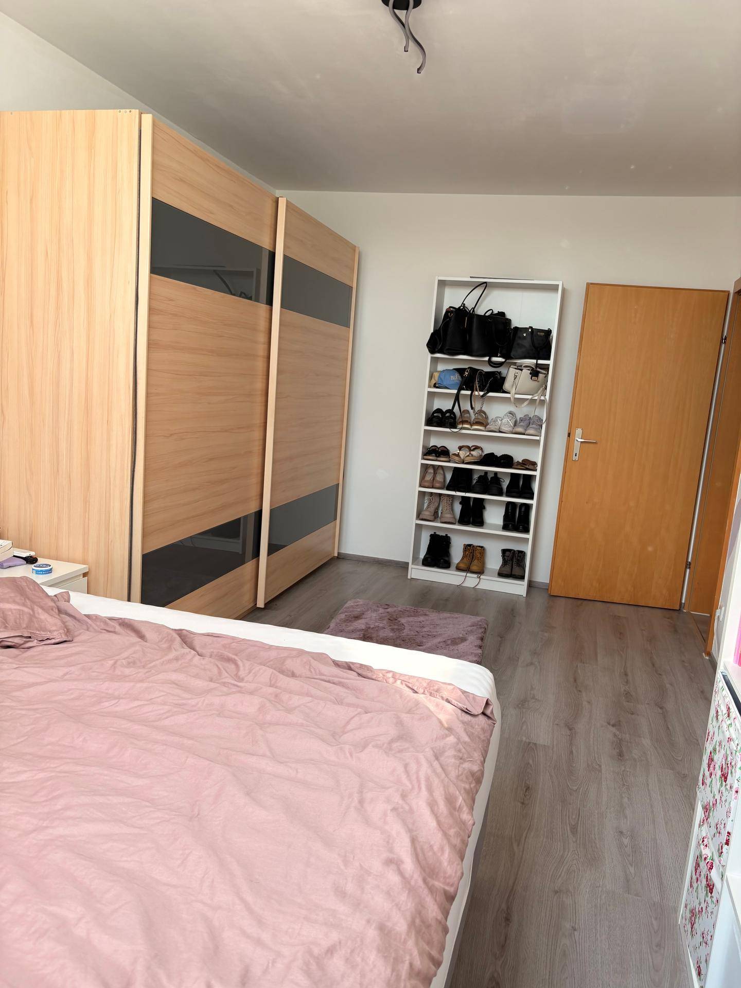 Schlafzimmer mit großem Schiebetürenschrank, Schuhregal und Laminatboden.